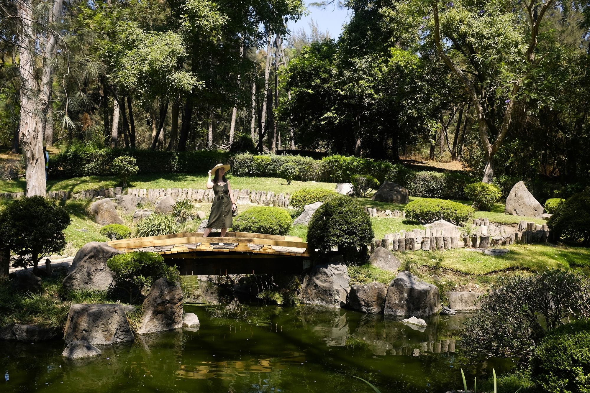 Alyssa stands on a bridge in the Japanese gardens wearing an olive dress