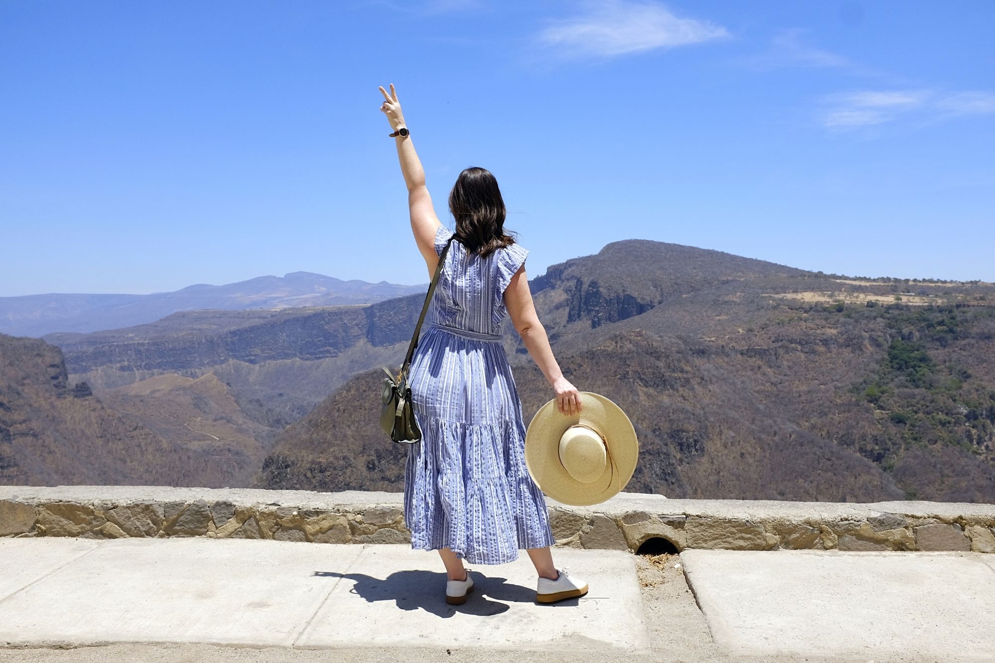 Alyssa holds a peace sign in the air and faces the canyon in Guadalajara