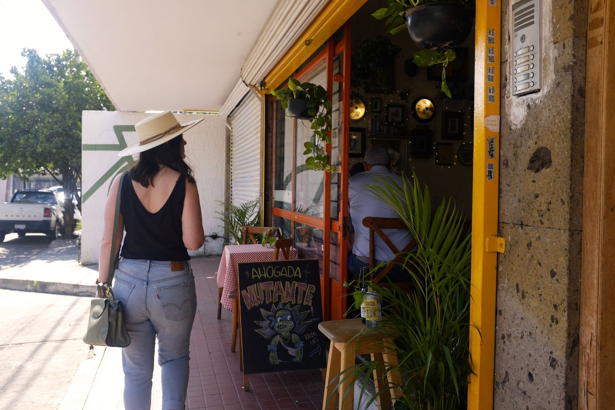 Alyssa walks by a restaurant wearing jeans, a tank, and a hat