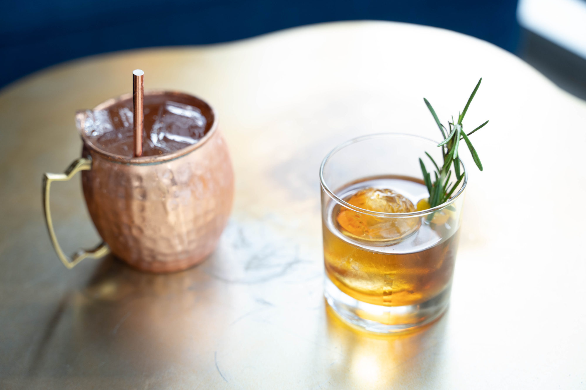 Two cocktails: a Moscow mule in a copper mug, and a bourbon/pear cocktail with a sprig of rosemary