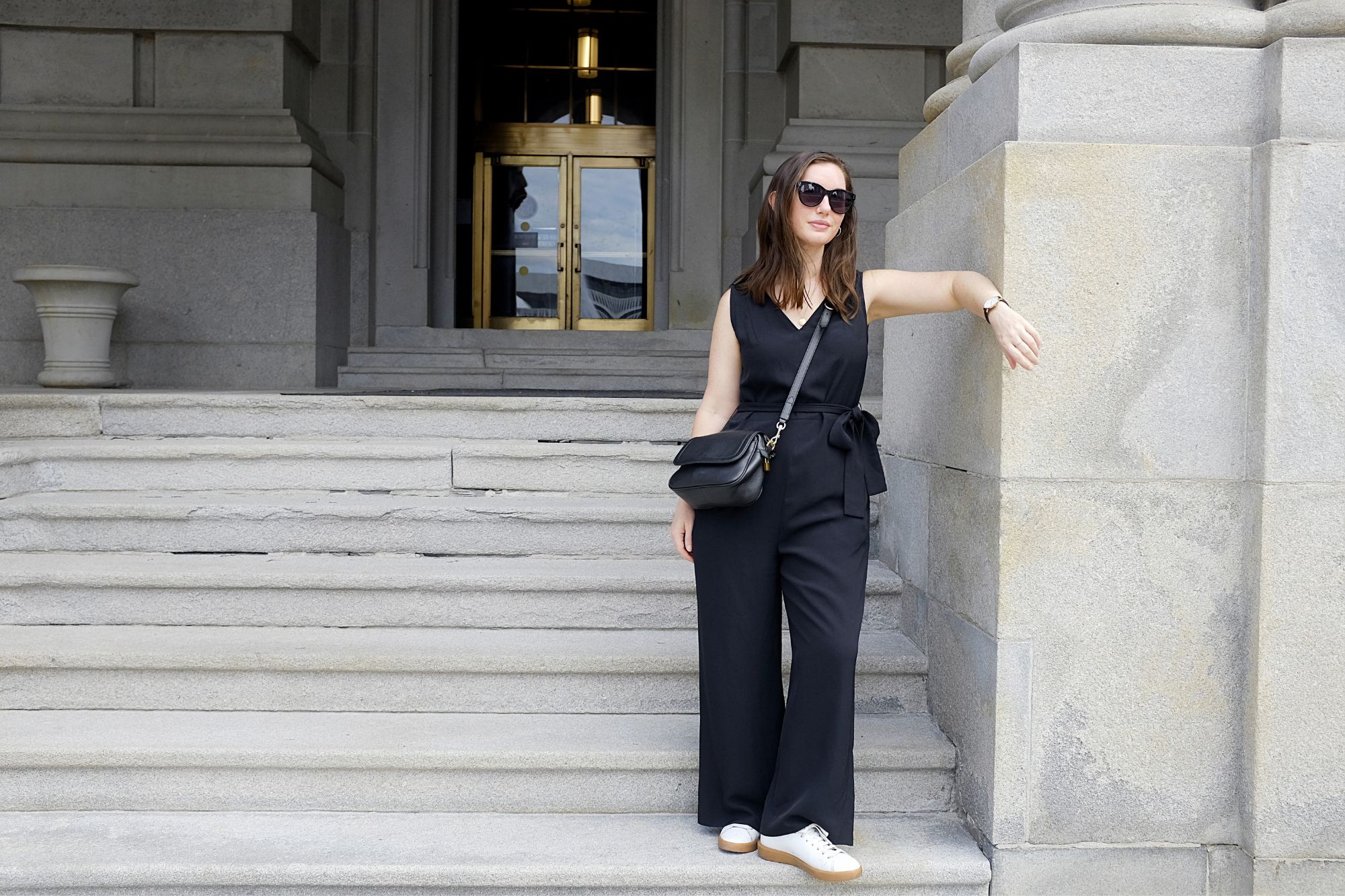 Alyssa stands by the NY State Capitol Building in a black jumpsuit