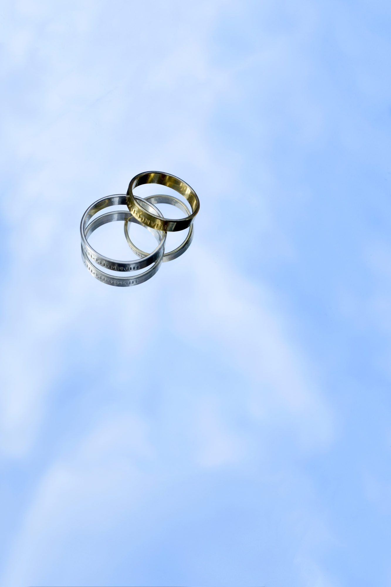 A gold and silver ring sit with the reflection of the sky below