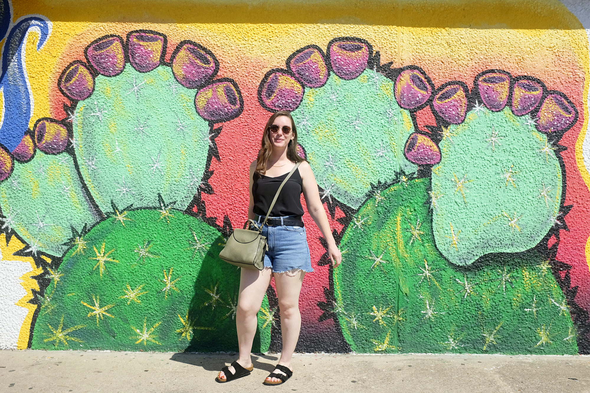 Alyssa stands in front of a catcus mural at Guapo Taco