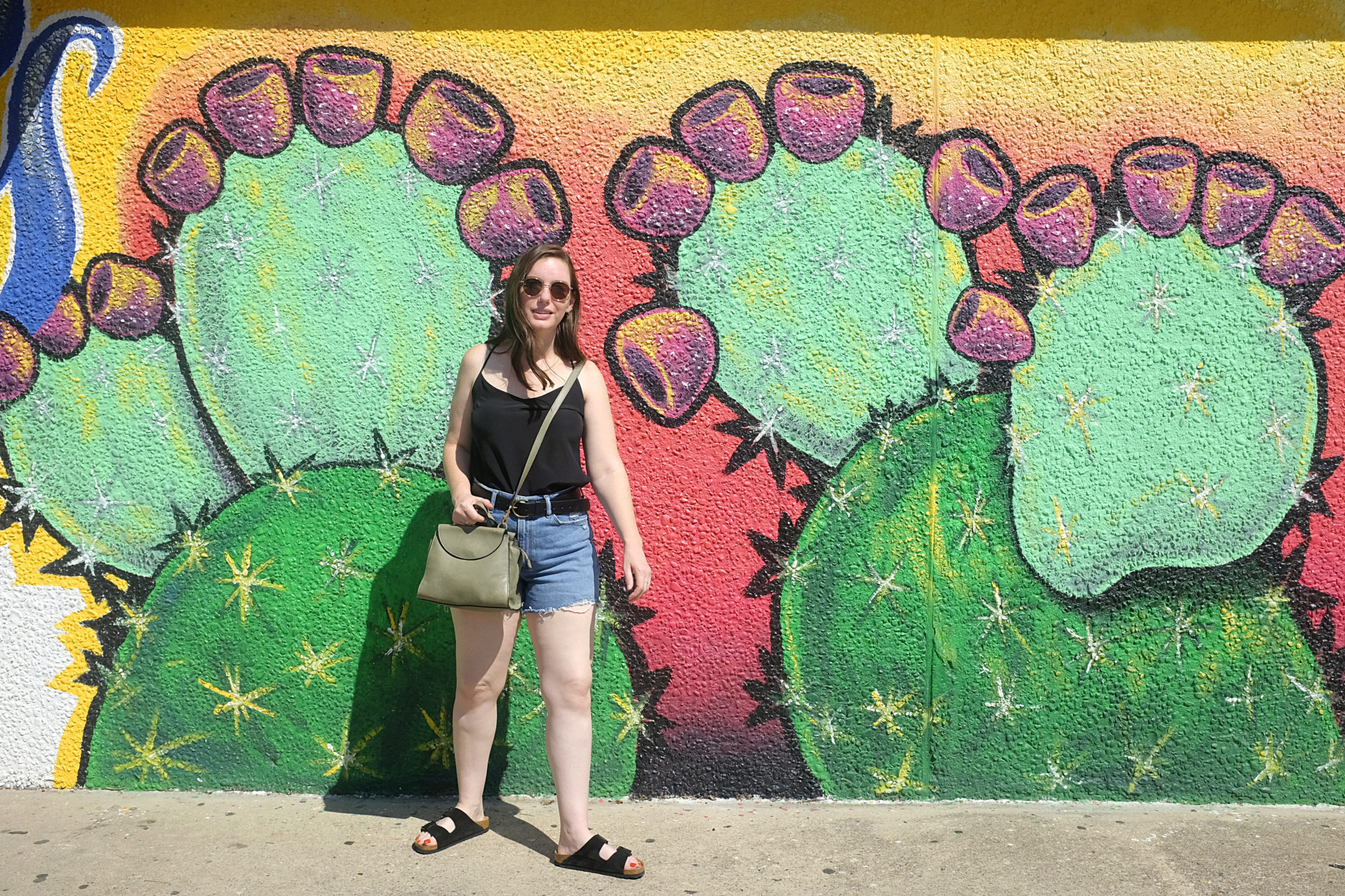 Alyssa wears a black silk tank, denim shorts, and black sandals