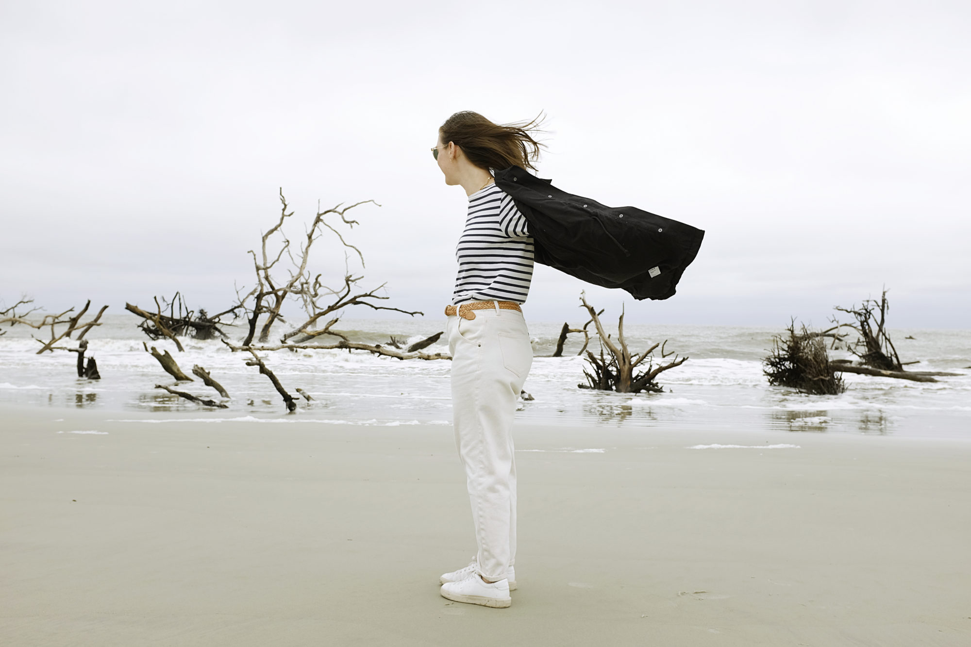 Alyssa stands on the beach with a jacket behind her blowing in the wind