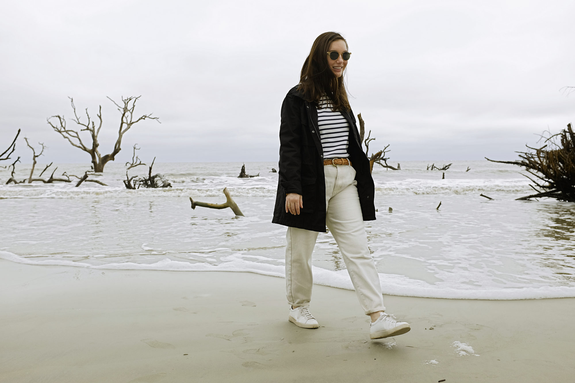 Alyssa walks on the beach in a white striped top and white jeans
