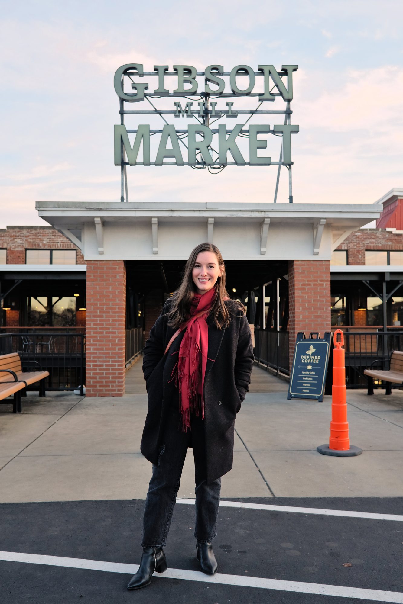 Alyssa wears a black sweater, jeans, and boots with a charcoal coat and red scarf