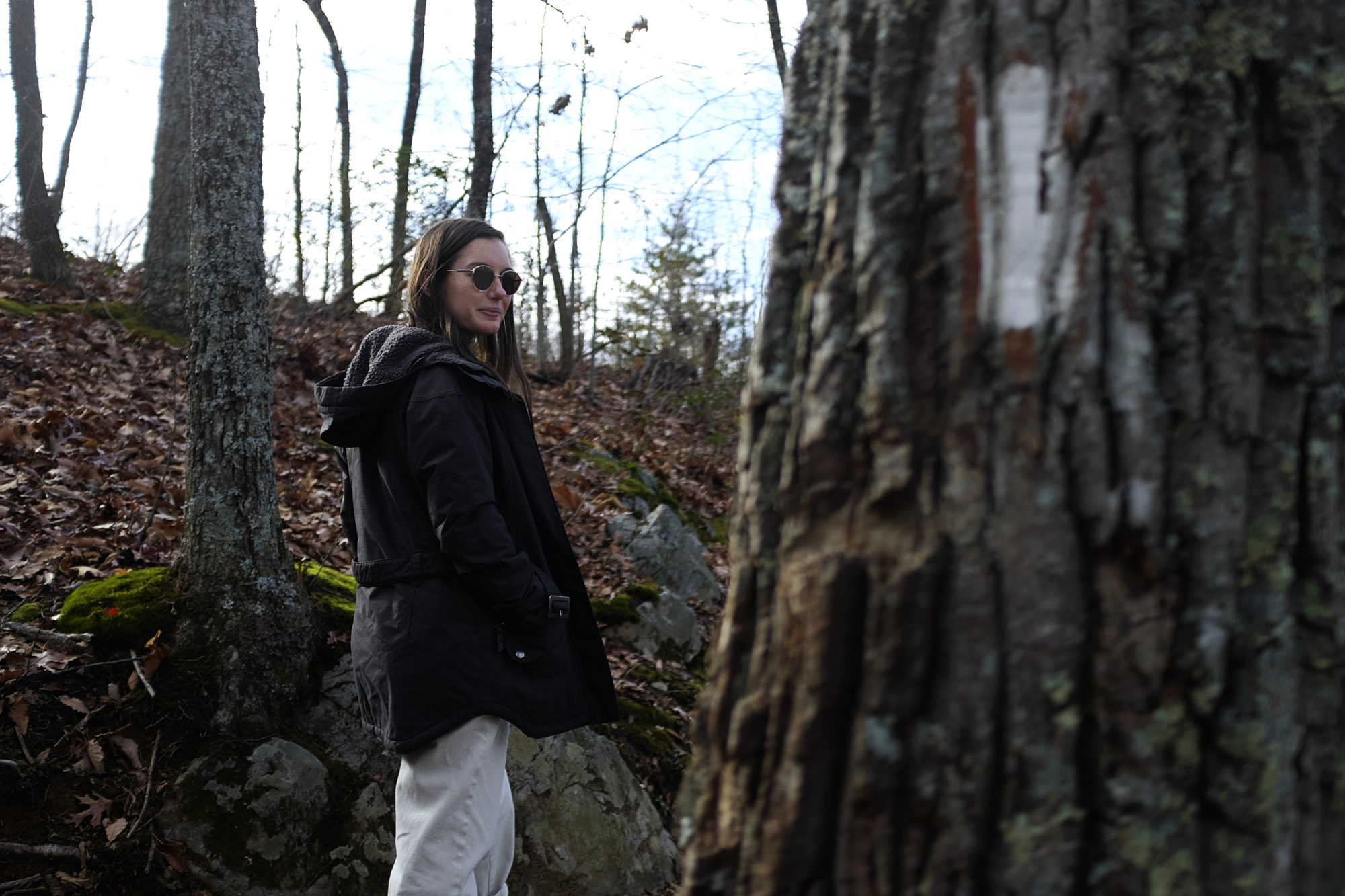 Alyssa hikes in Johnson City wearing a jacket, boots, and white pants. She is looking back at the camera, and a white trail blaze is visible