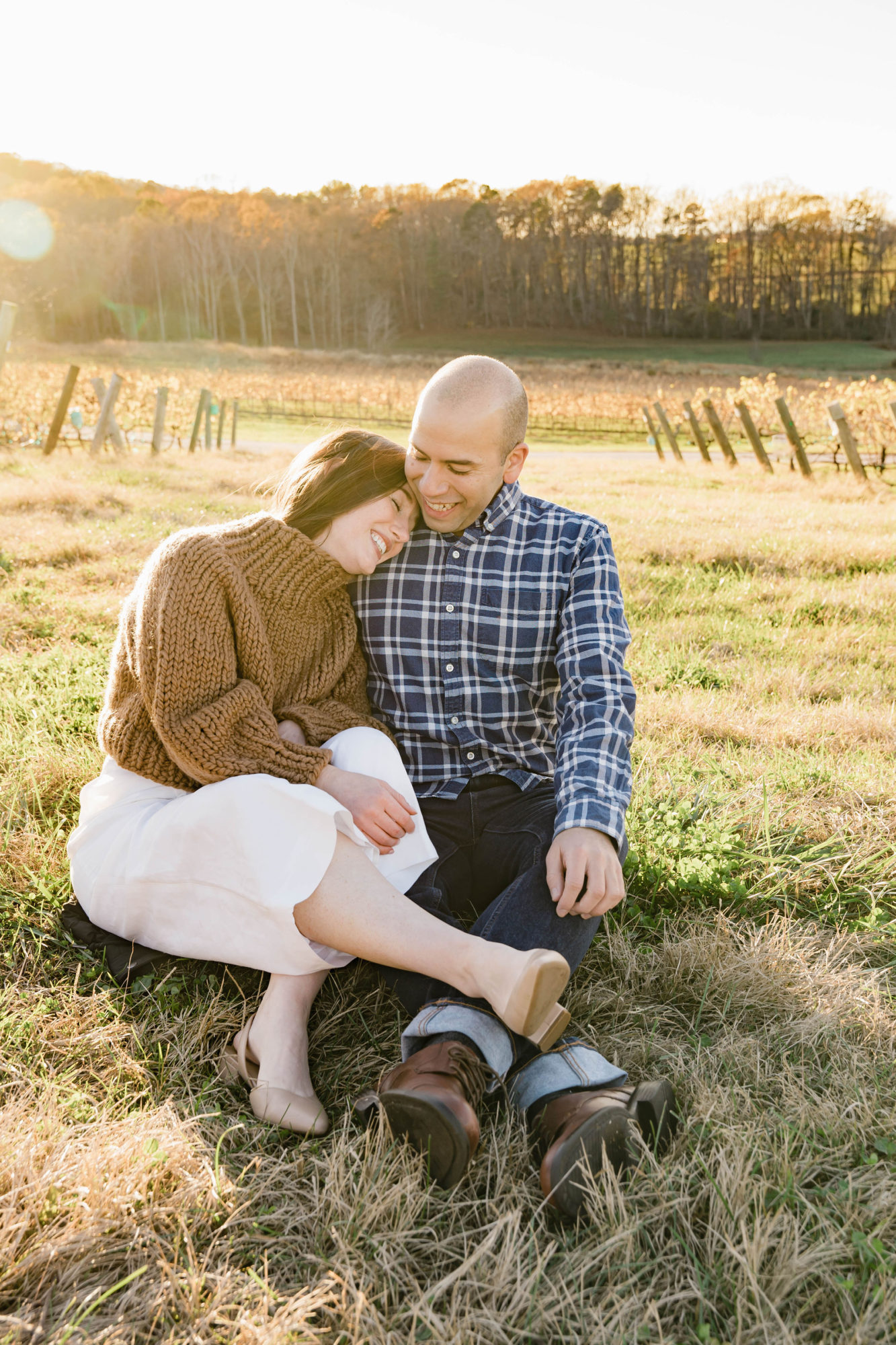 Alyssa and Michael sit on the ground at a winery, snuggled up together