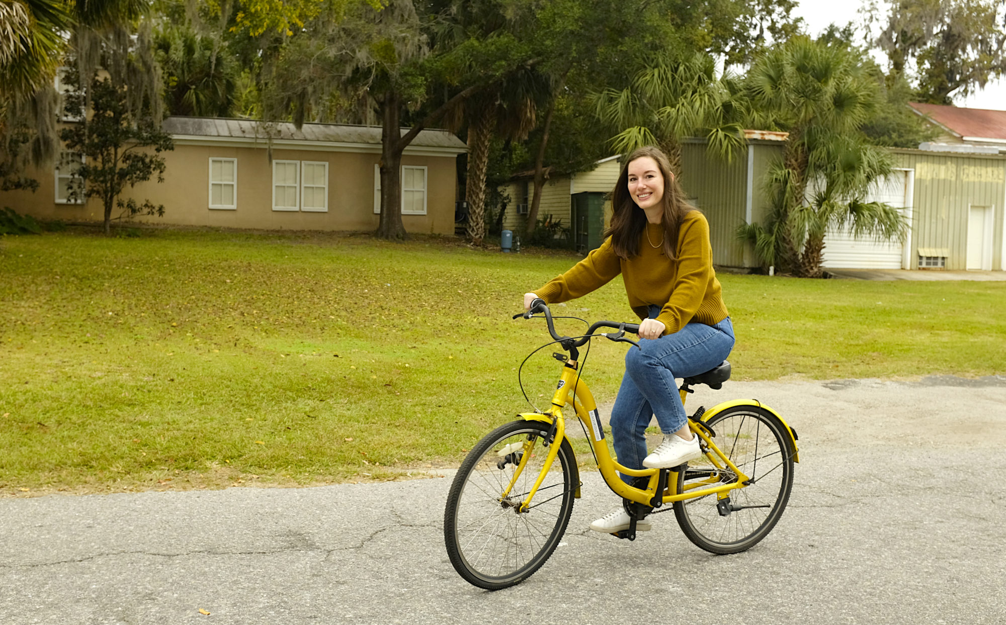 Alyssa rides a bike in a green sweater and blue jeans