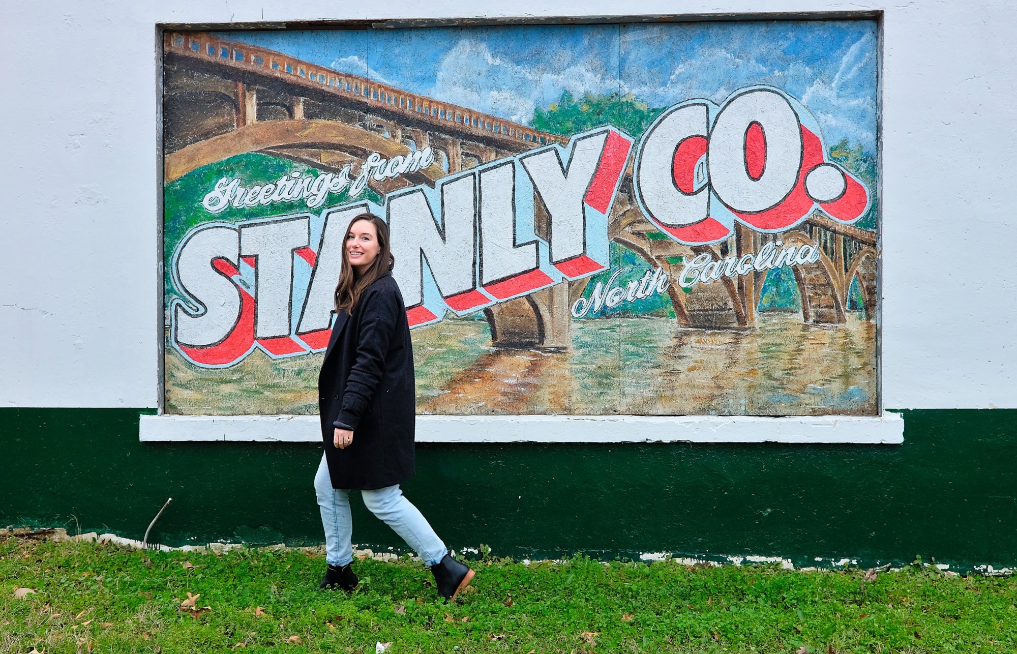 Alyssa walks in front of a mural that reads "Greetings from Stanly Co." in Albemarle