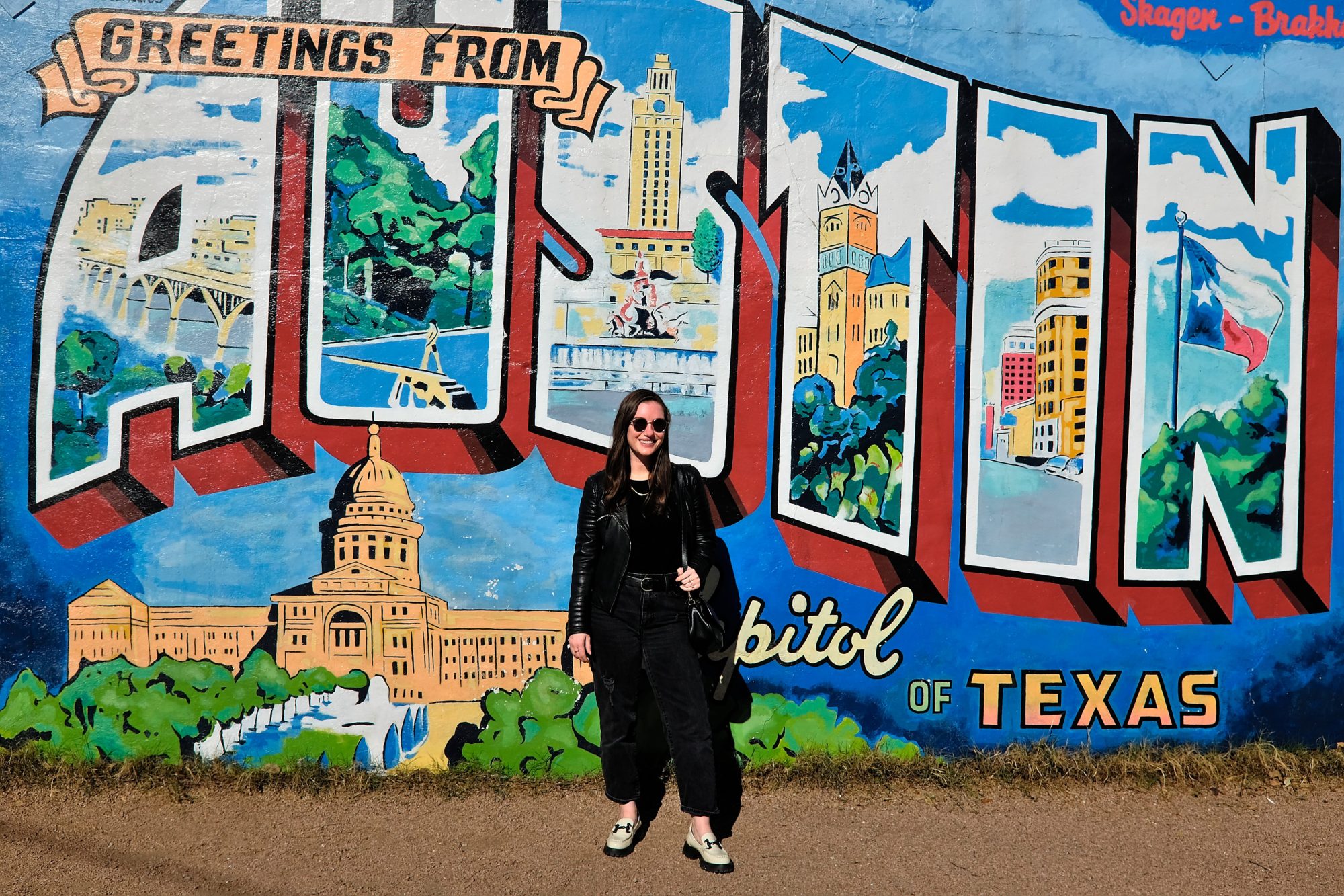 Alyssa stands in front of the Greetings from Austin Mural