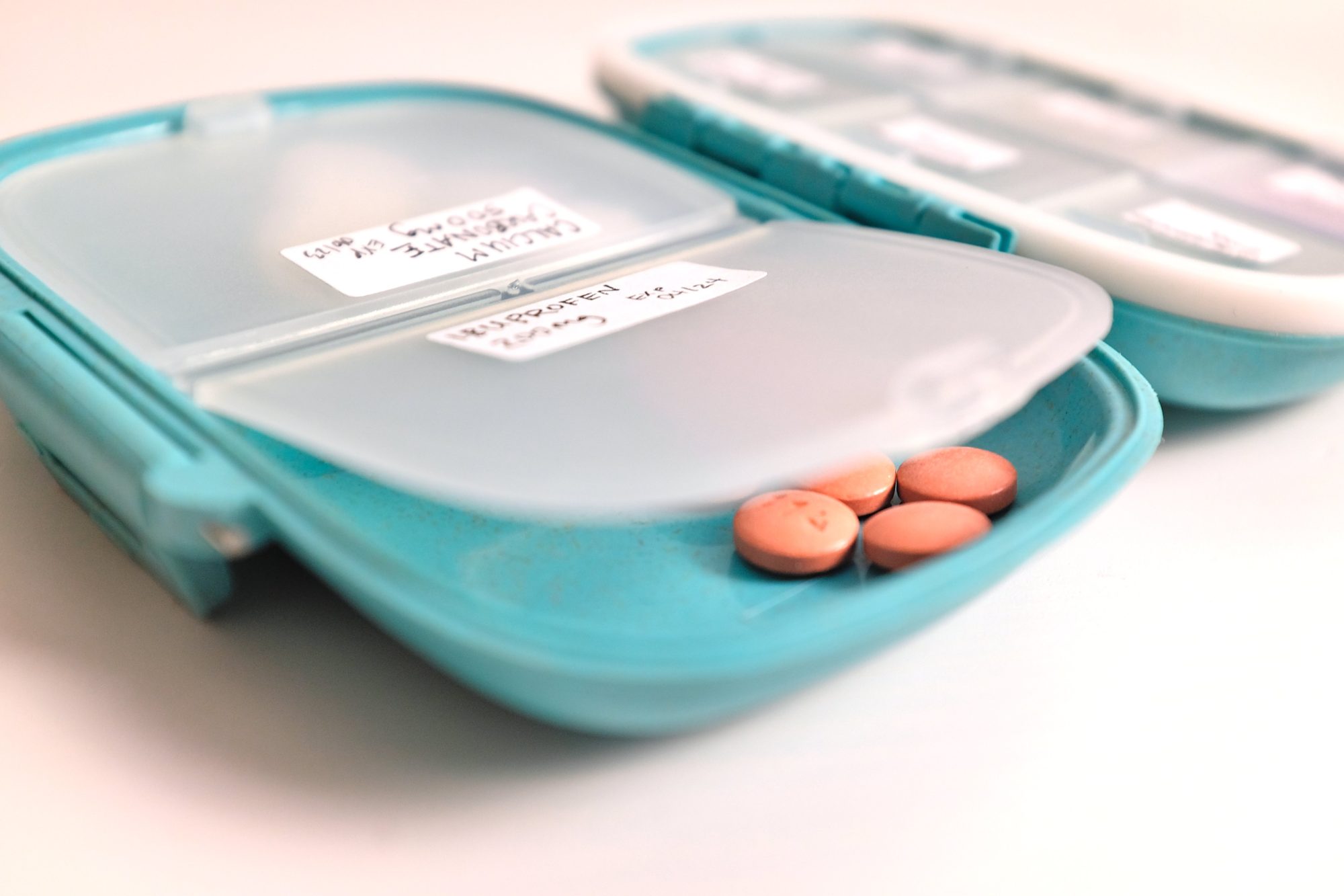 An open travel pillbox containing over the counter medications and supplements