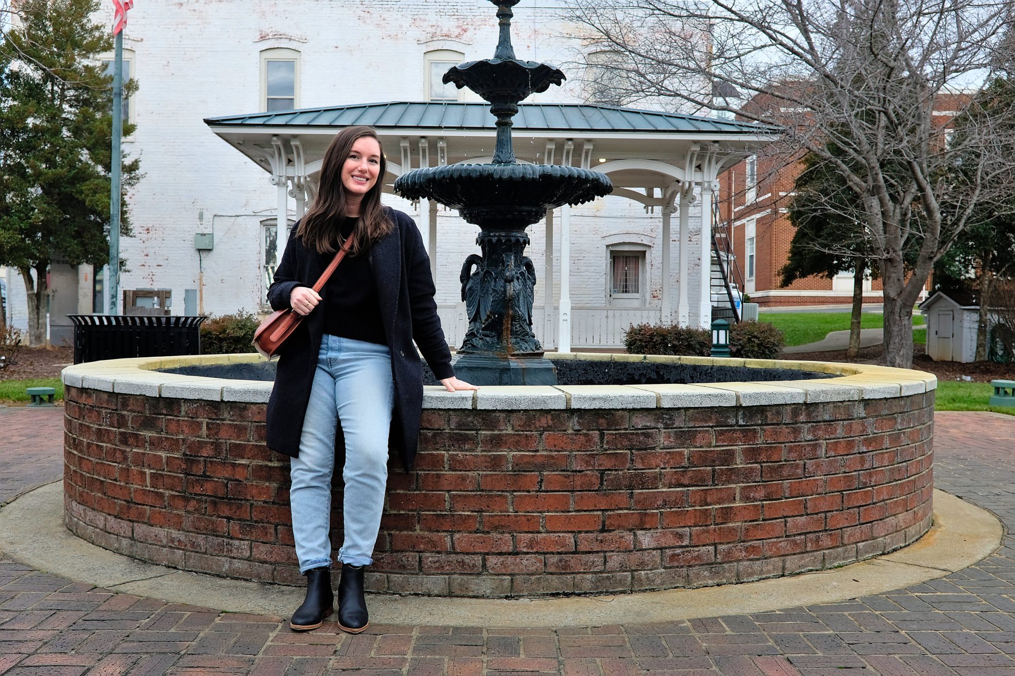 Alyssa wears blue jeans and a black sweater, boots, and coat