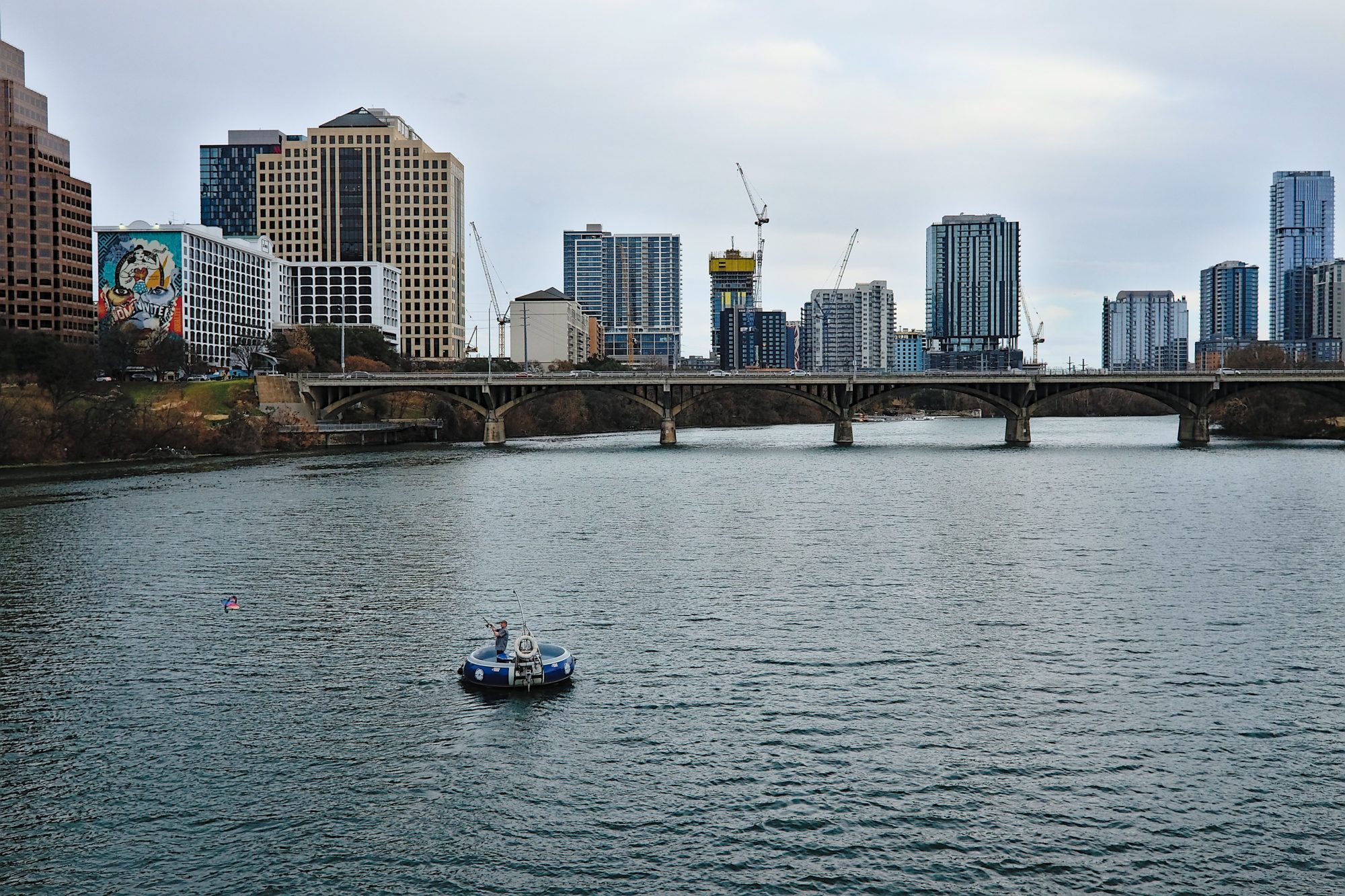 View of the Colorado River from a bridge in Austin with a masculine-presenting person flying a kite