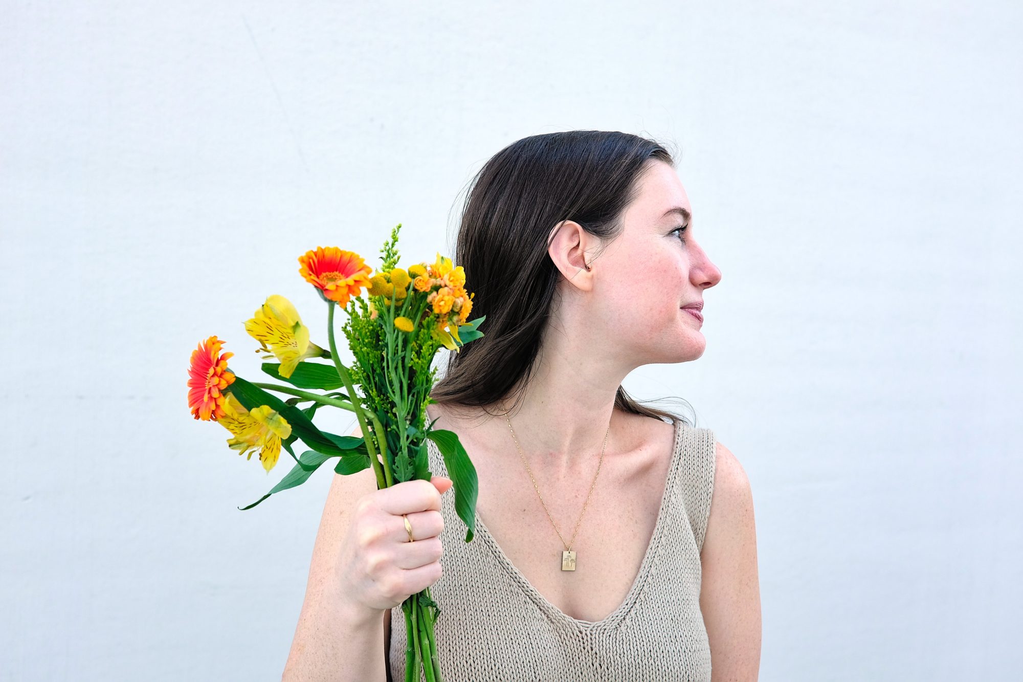 Alyssa holds a bouquet of flowers while wearing GLDN jewelry and looks away from the camera