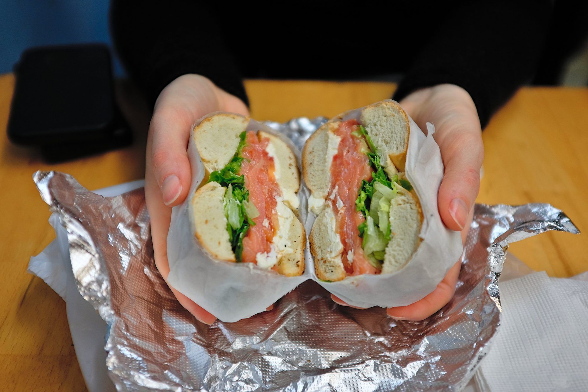 Alyssa cracks open a nova lox bagel sandwich at Heaven's Hot Bagels