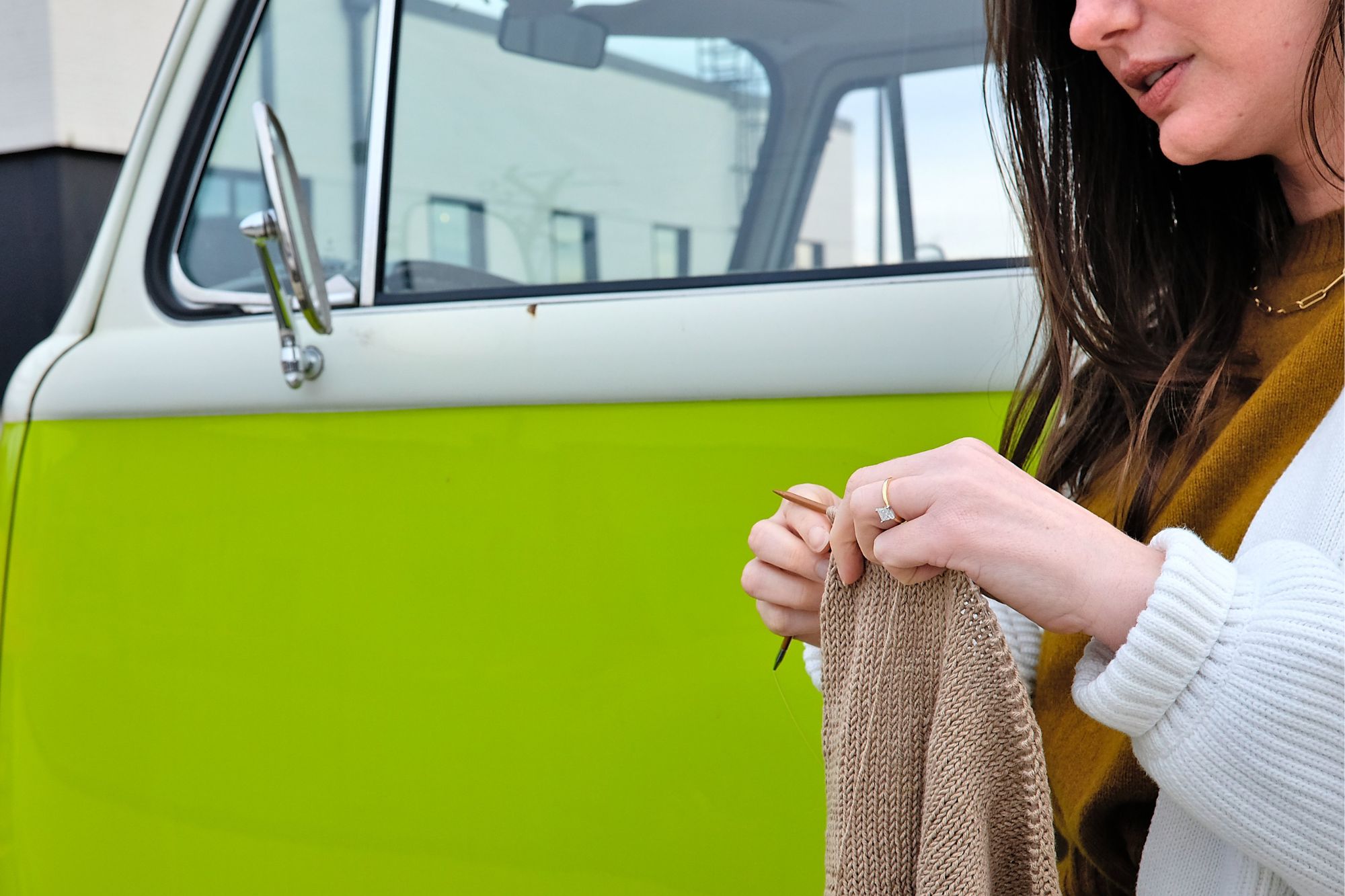 Alyssa stands outside of a VW bus and knits