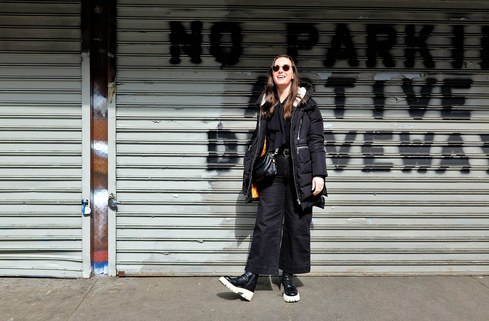 Alyssa wears a big coat over an all-black outfit