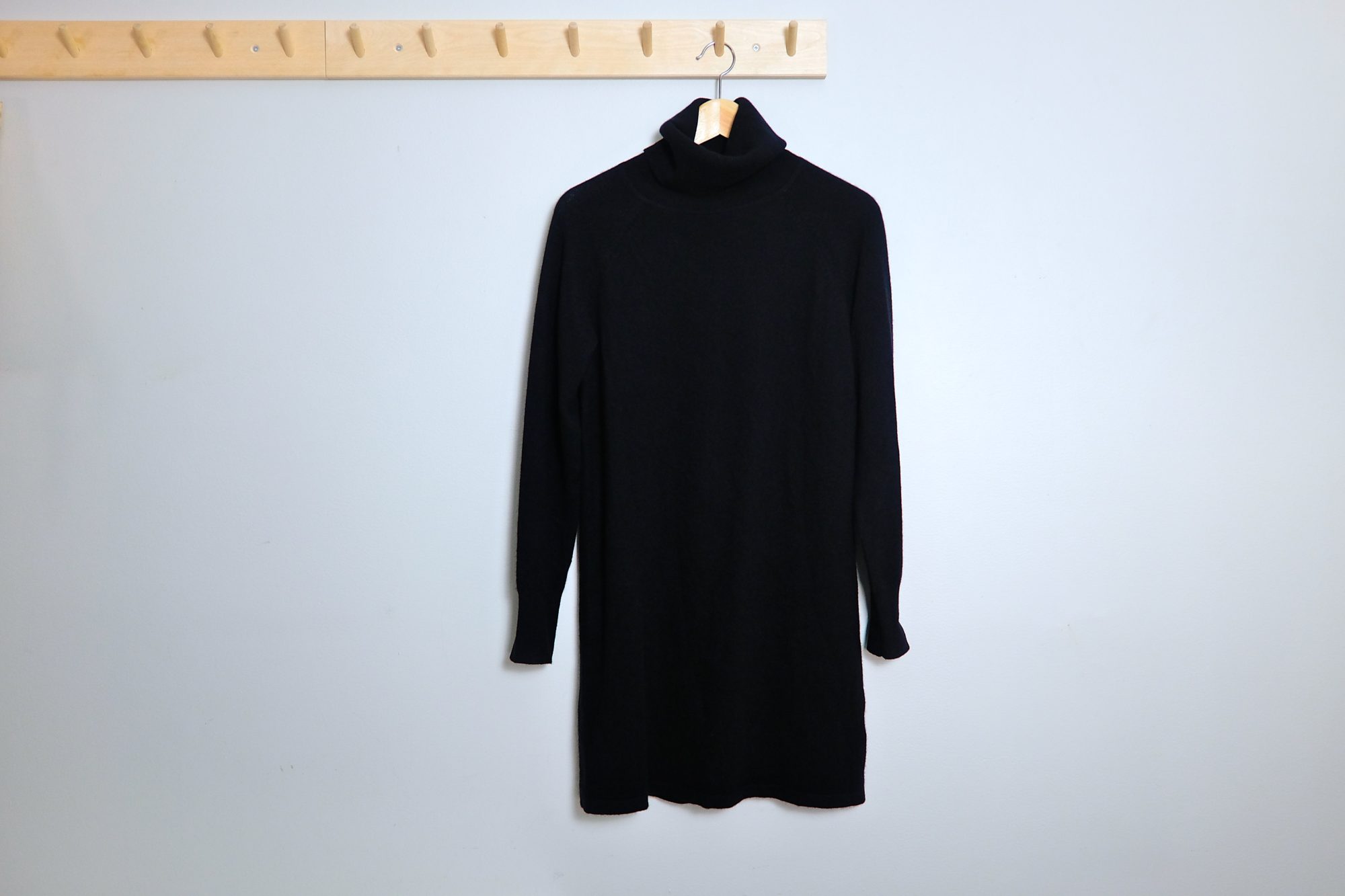 A black cashmere dress hangs on a peg rack