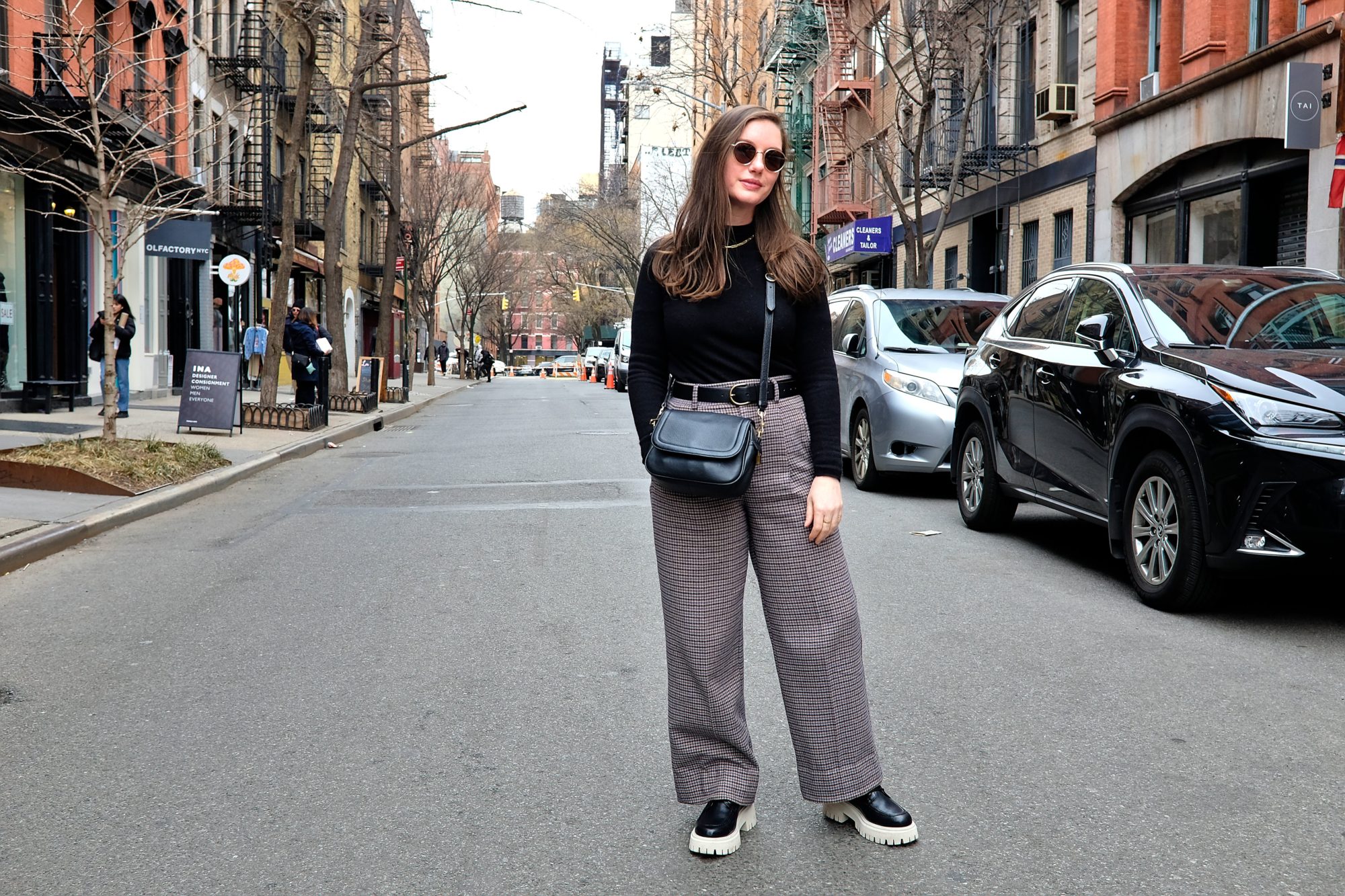 Alyssa stands on a street in NYC wearing a black sweater and wool pants
