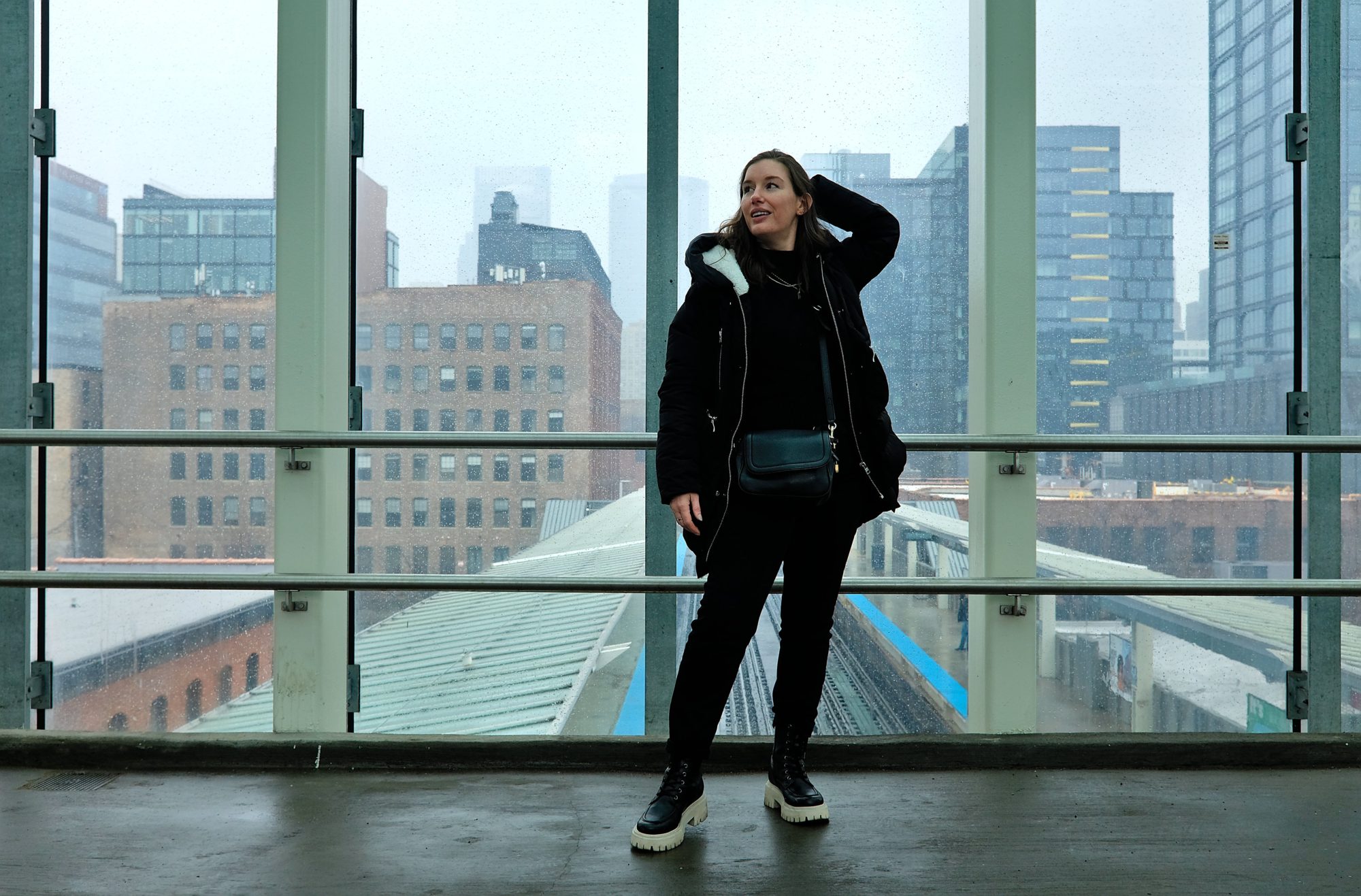 Alyssa stands on a platform over the L tracks wearing all black