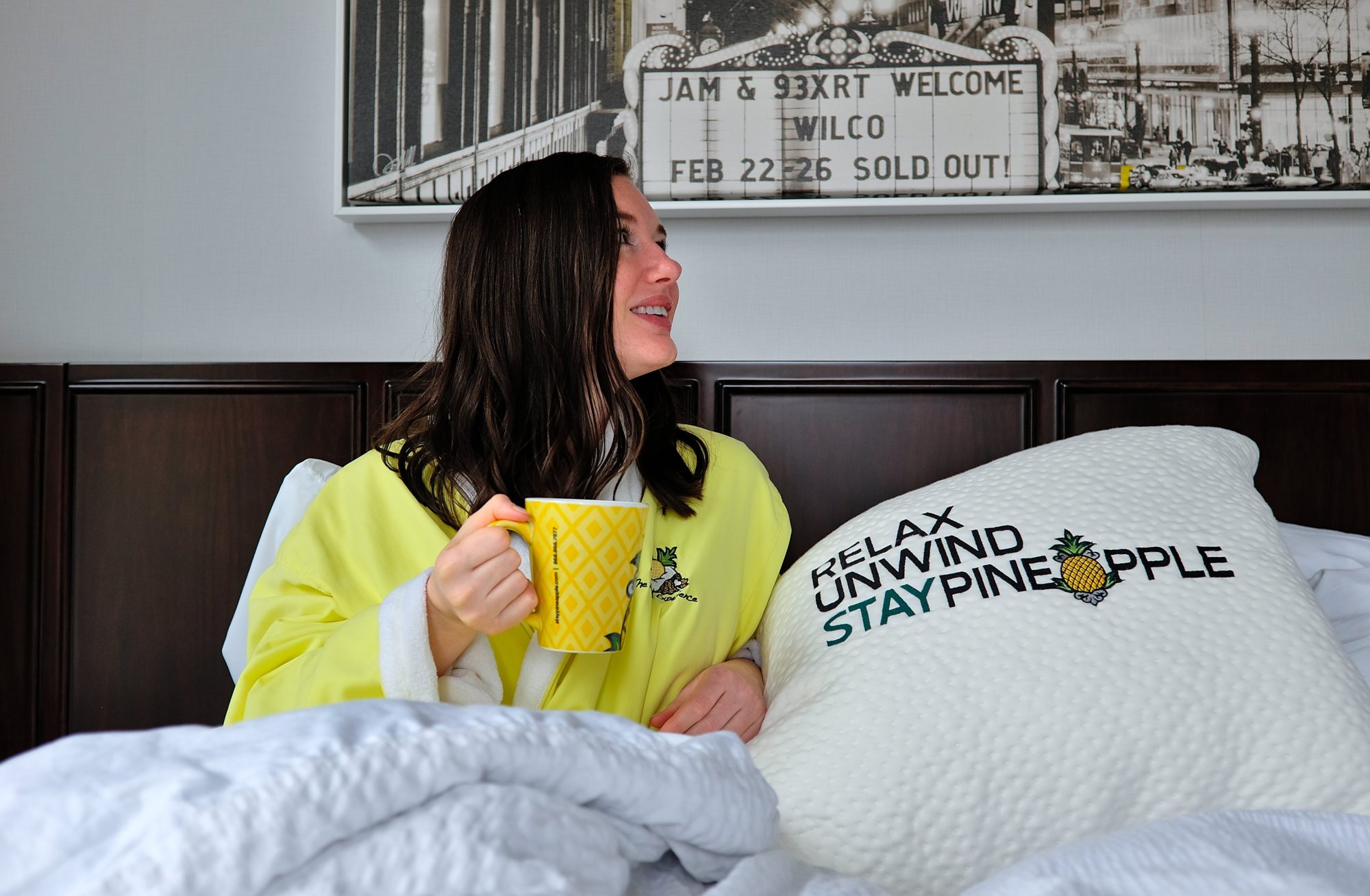 Alyssa wears a yellow robe and holds a cup of coffee while in the bed