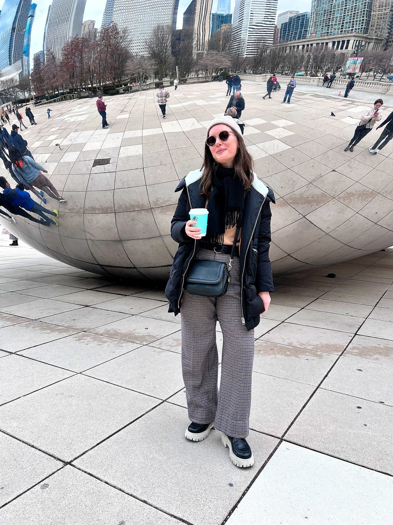 Alyssa wears wool pants and a camel sweater with a big coat in front of The Bean
