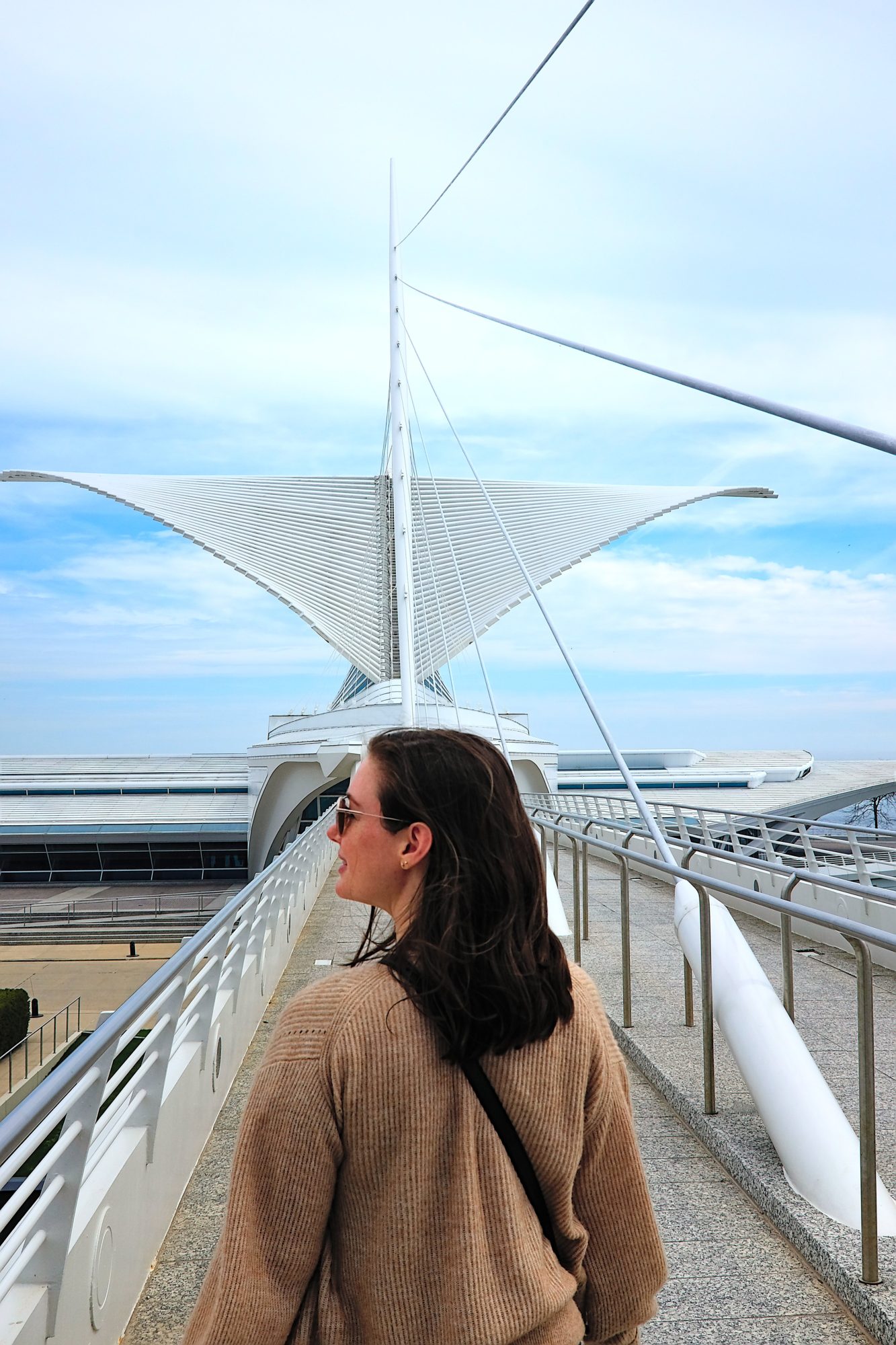 Alyssa walks in front of the Milwaukee Art Museum wearing a tan sweater