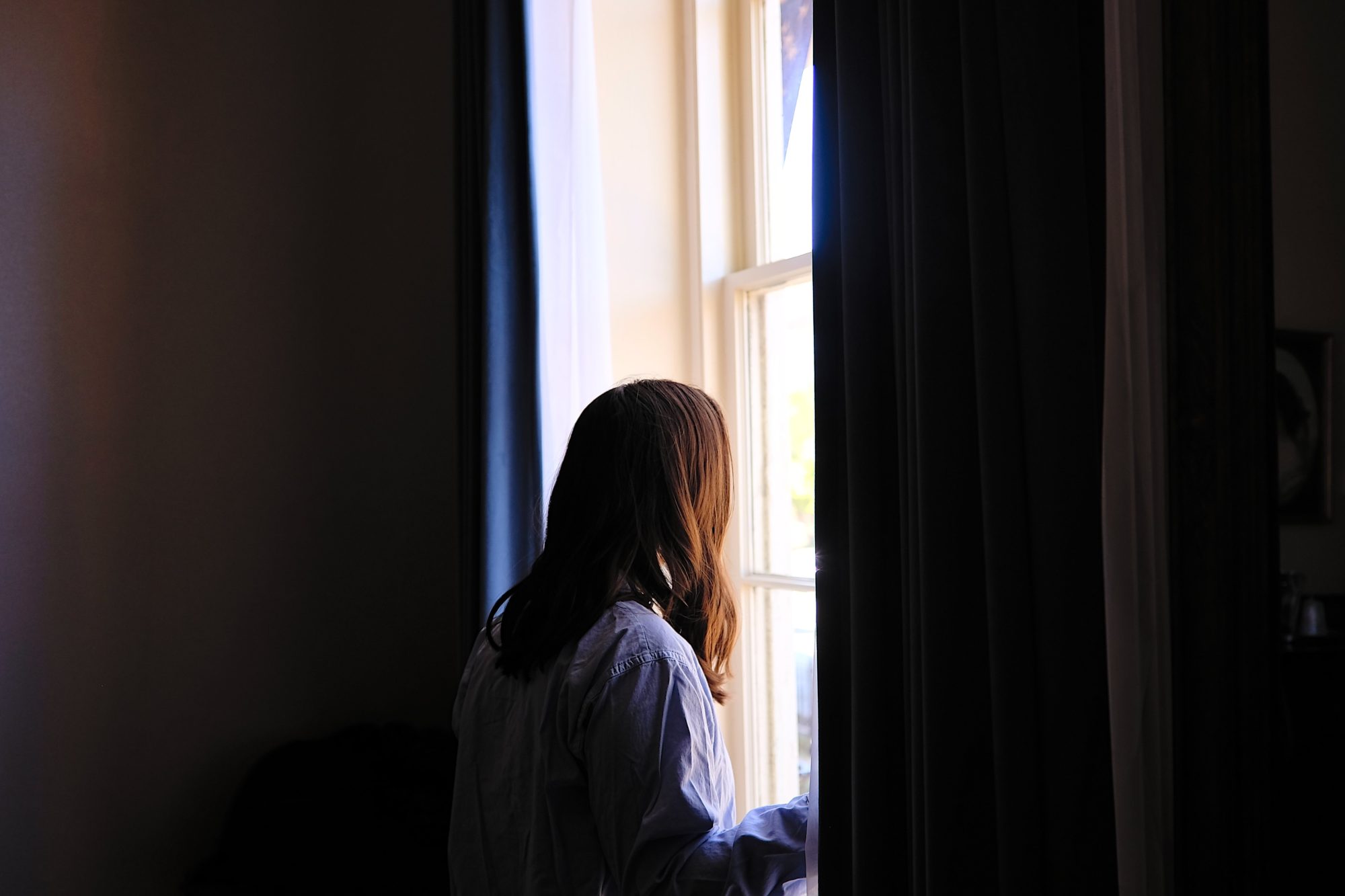 Alyssa wears a blue sleep shirt and peers out the window