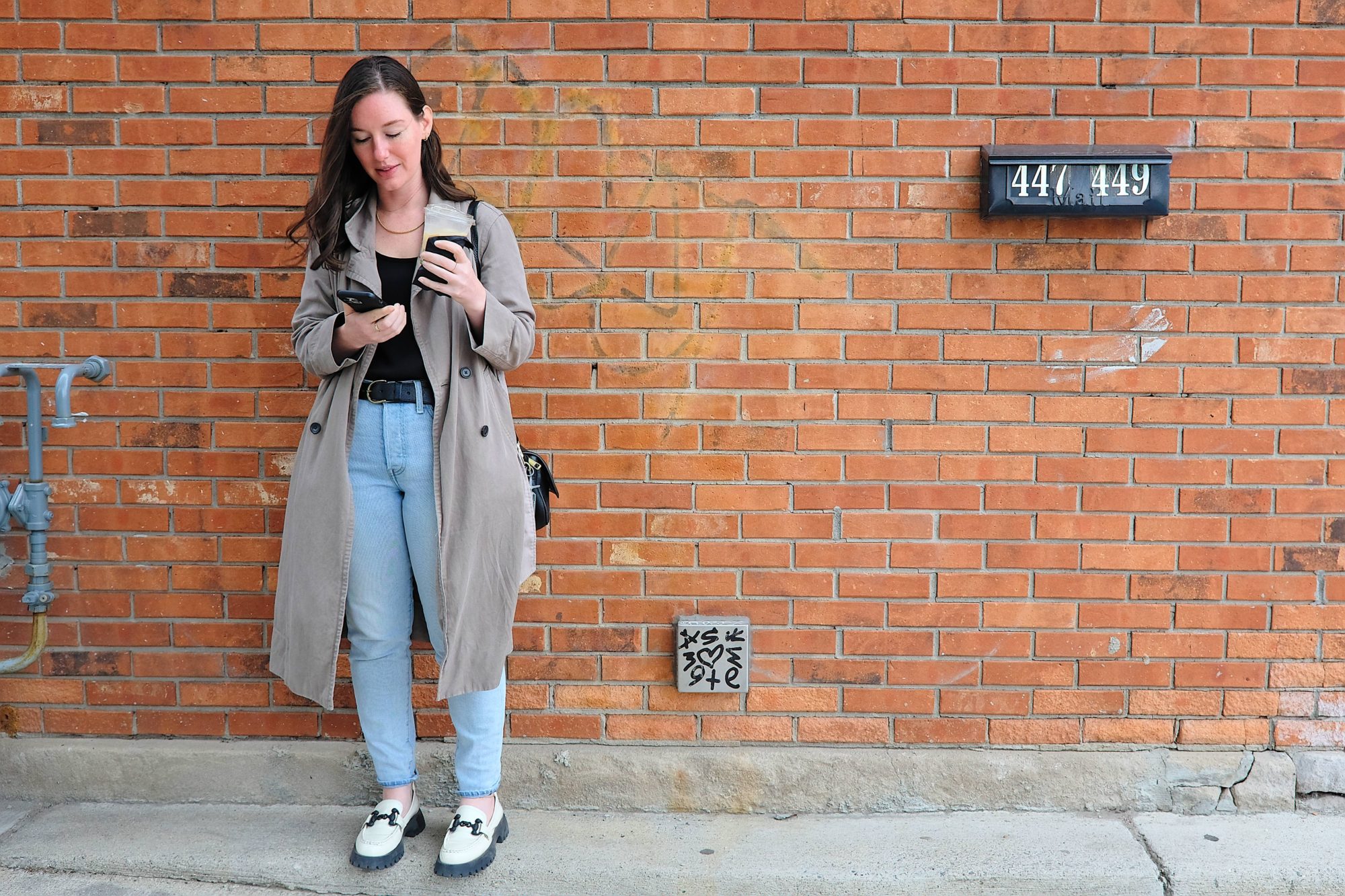 Alyssa wears a black silk tank, blue jeans, loafers, and trench