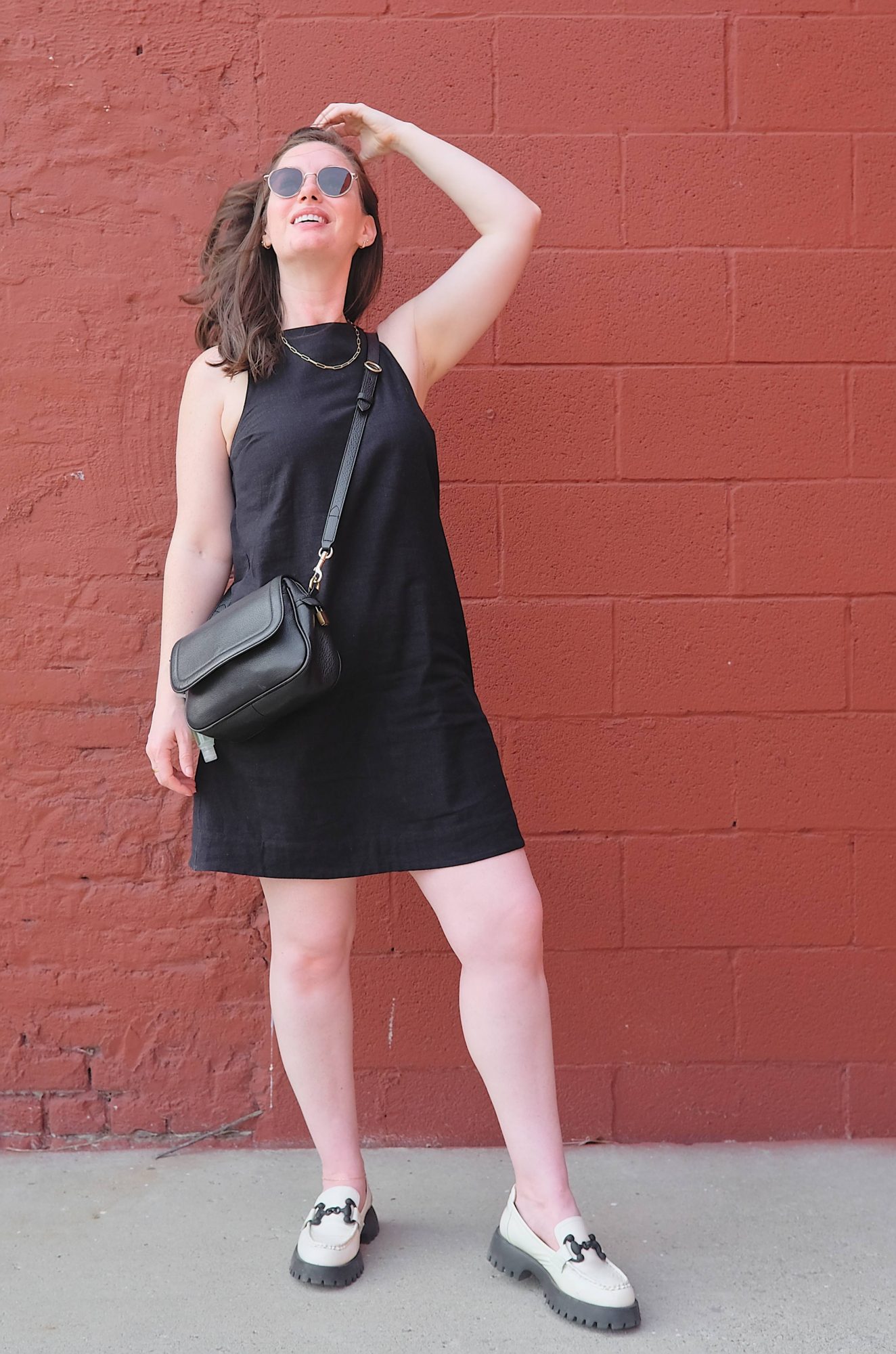 Alyssa wears a black dress and stands in front of a red wall
