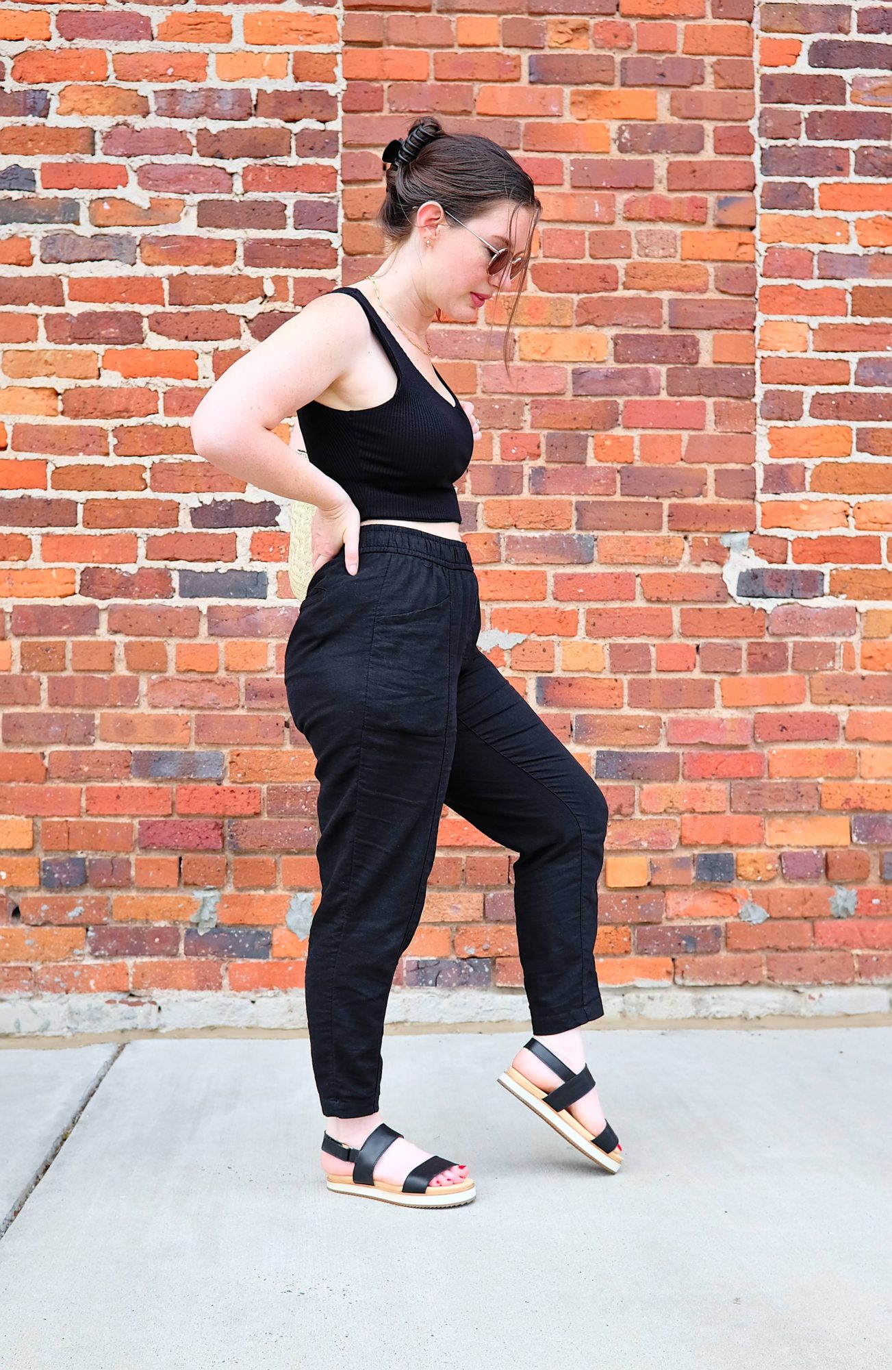 Alyssa wears a crop top, linen pants, and the Nisolo sandals while turning to one side