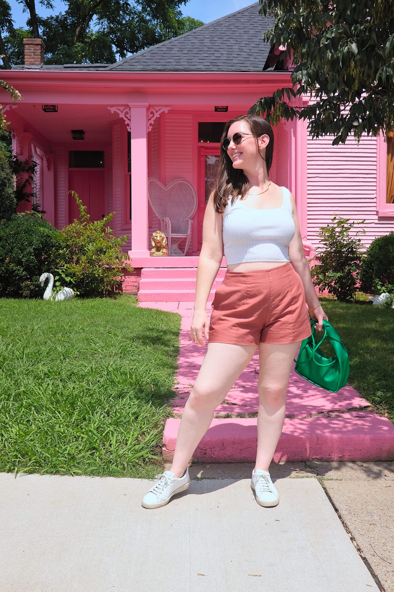 Alyssa wears a white top and rust shorts in front of a pink house
