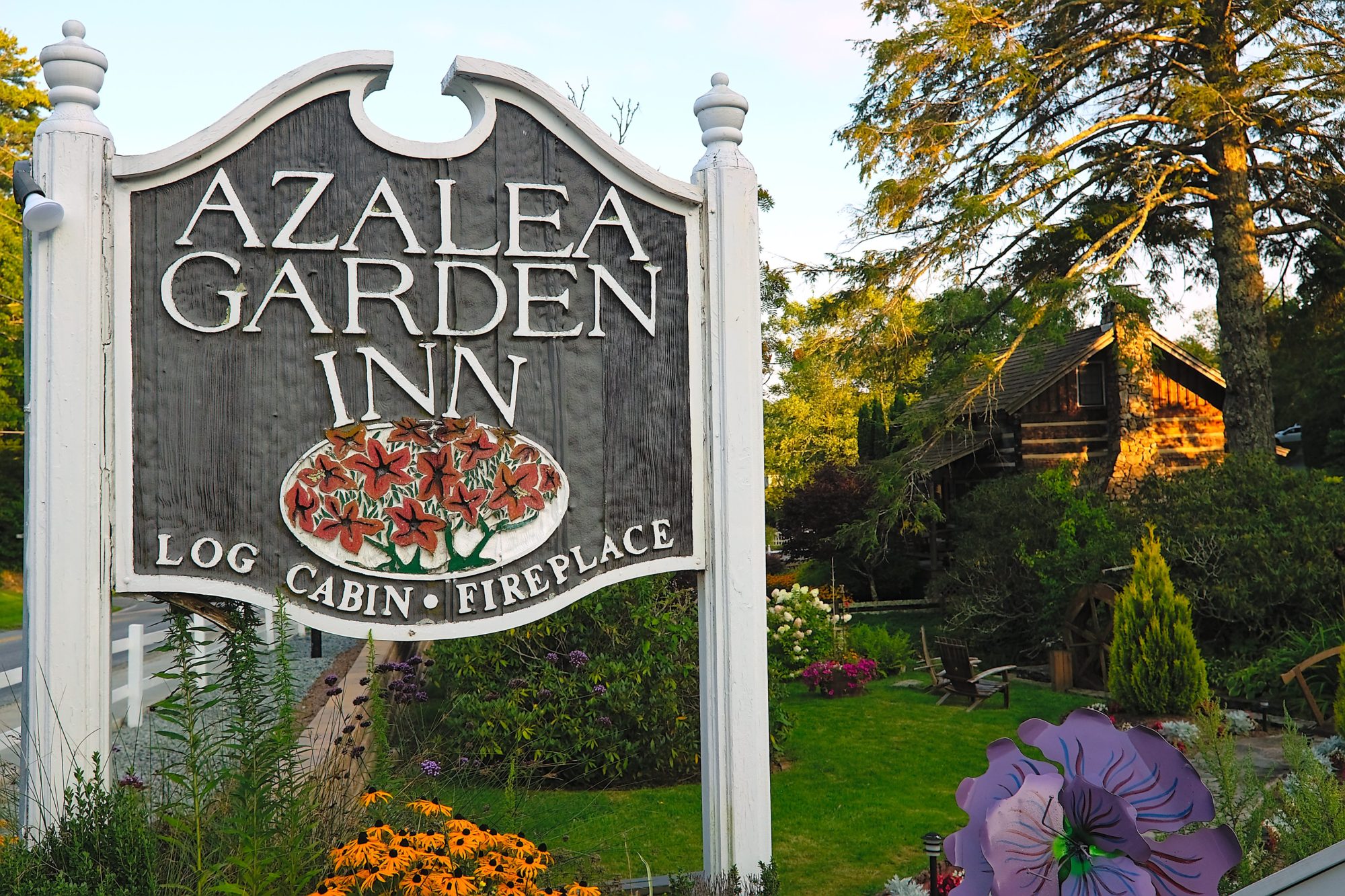 The sign for the Azalea Garden Inn with the log cabin in the background