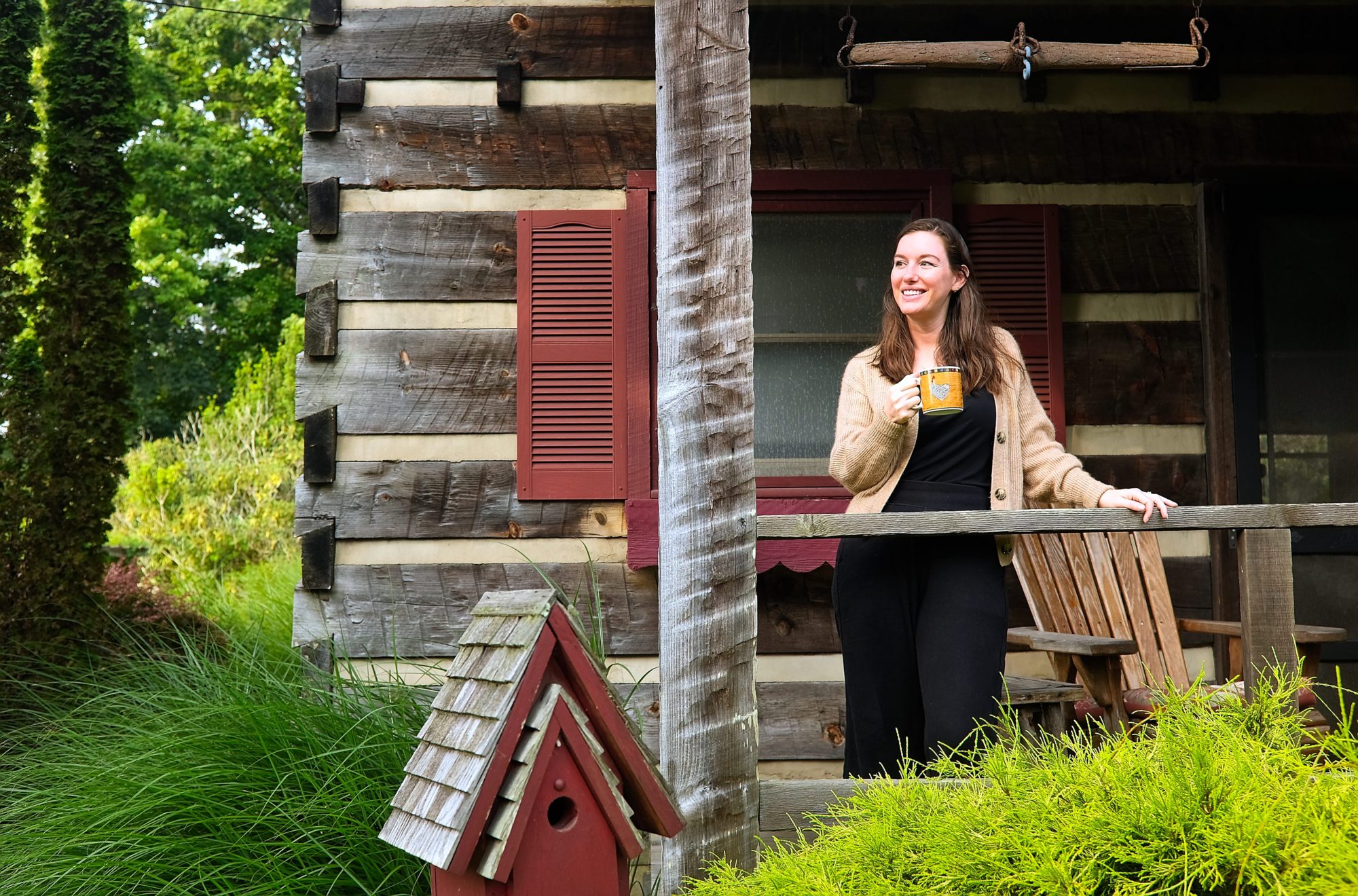 Alyssa on the porch of the log cabin with a mug