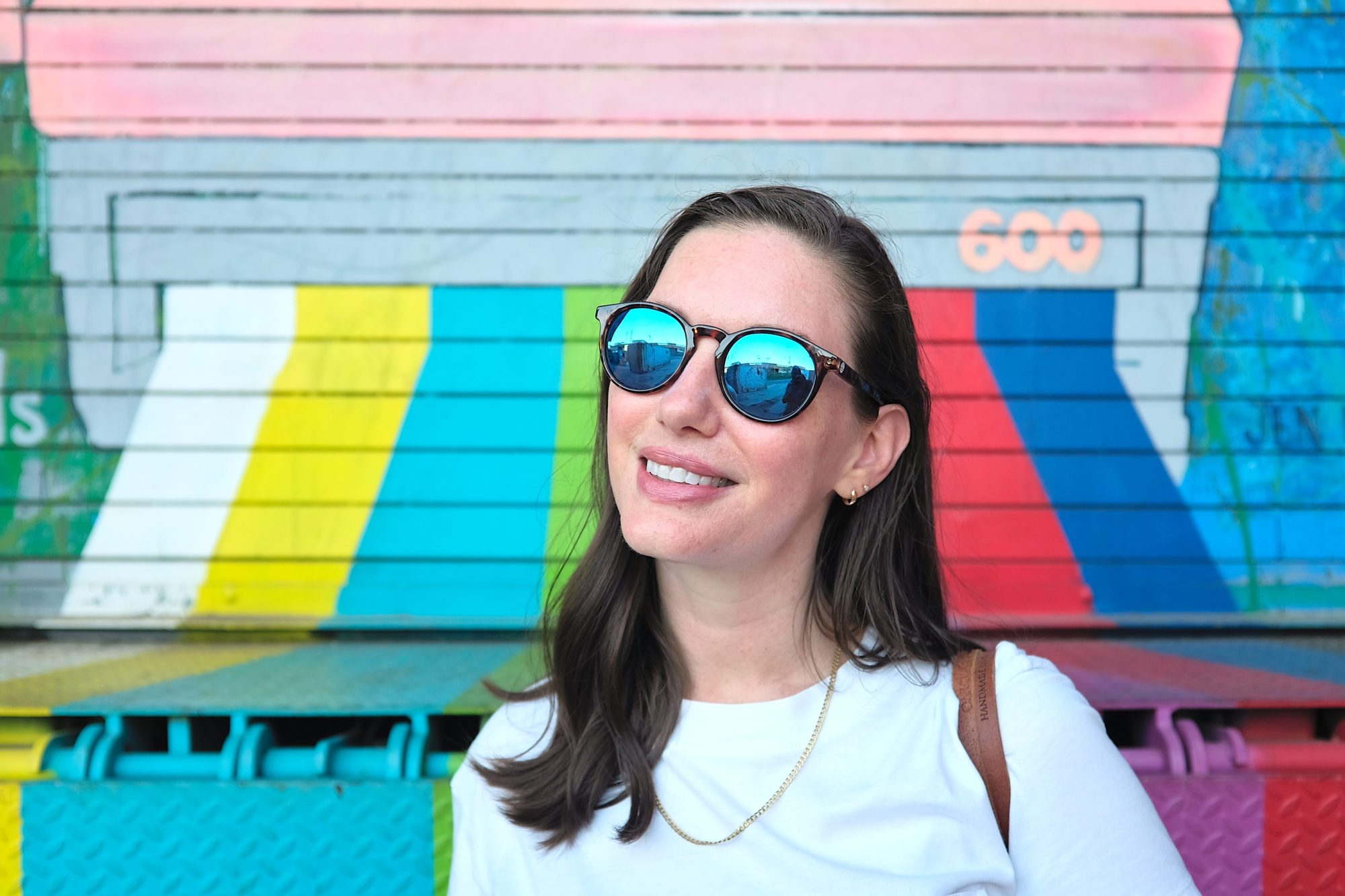 Alyssa wears the Sunski Dipsea sunglasses in front of a colorful background