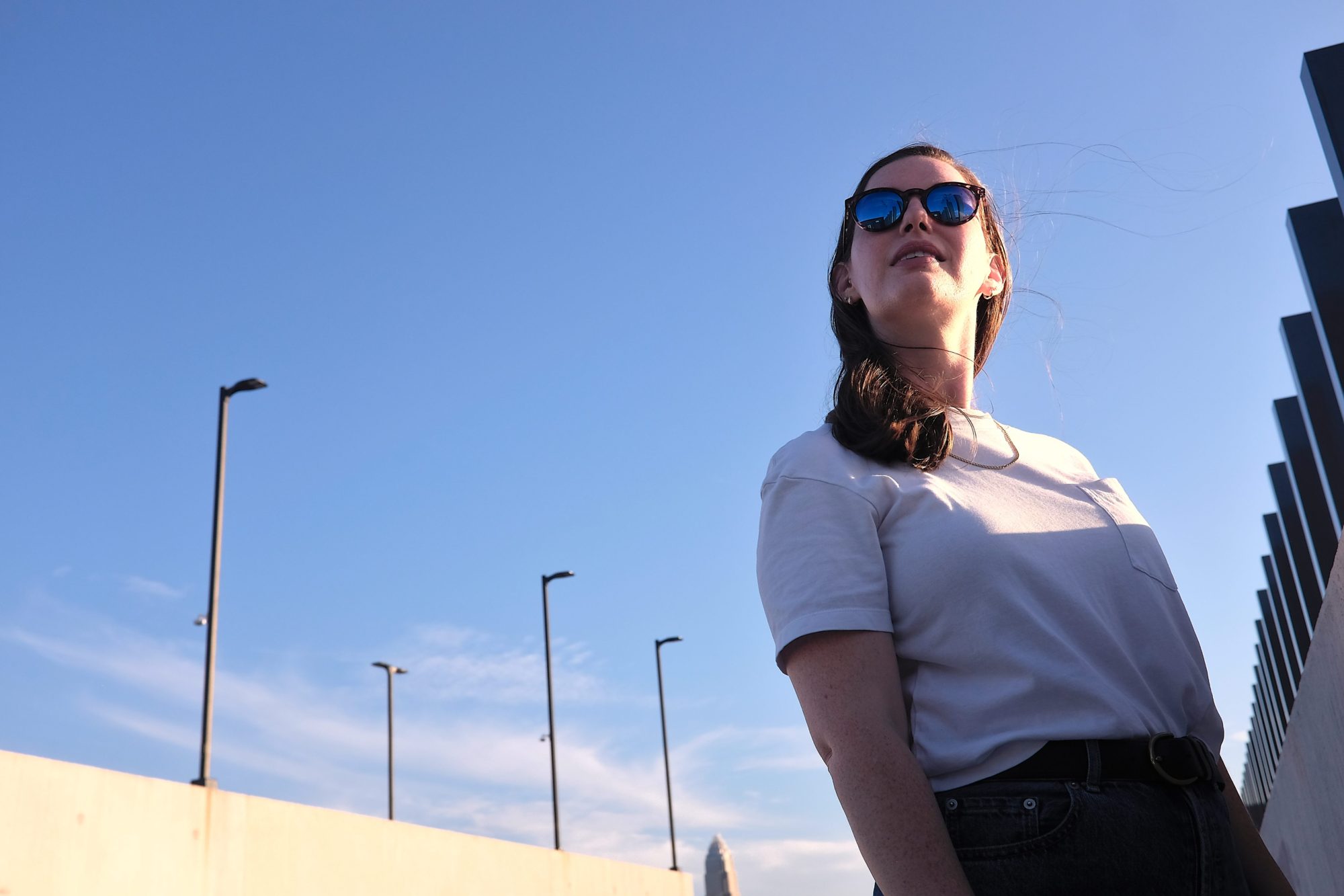 Alyssa wears the Sunski Dipsea sunglasses with a white tee and jeans on the roof of a parking deck