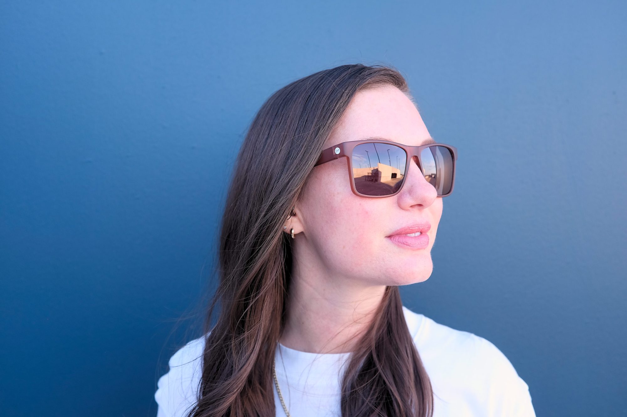 Alyssa wears the Sunski Puerto sunglasses in Sienna Ruby in front of a blue wall and turns to her left