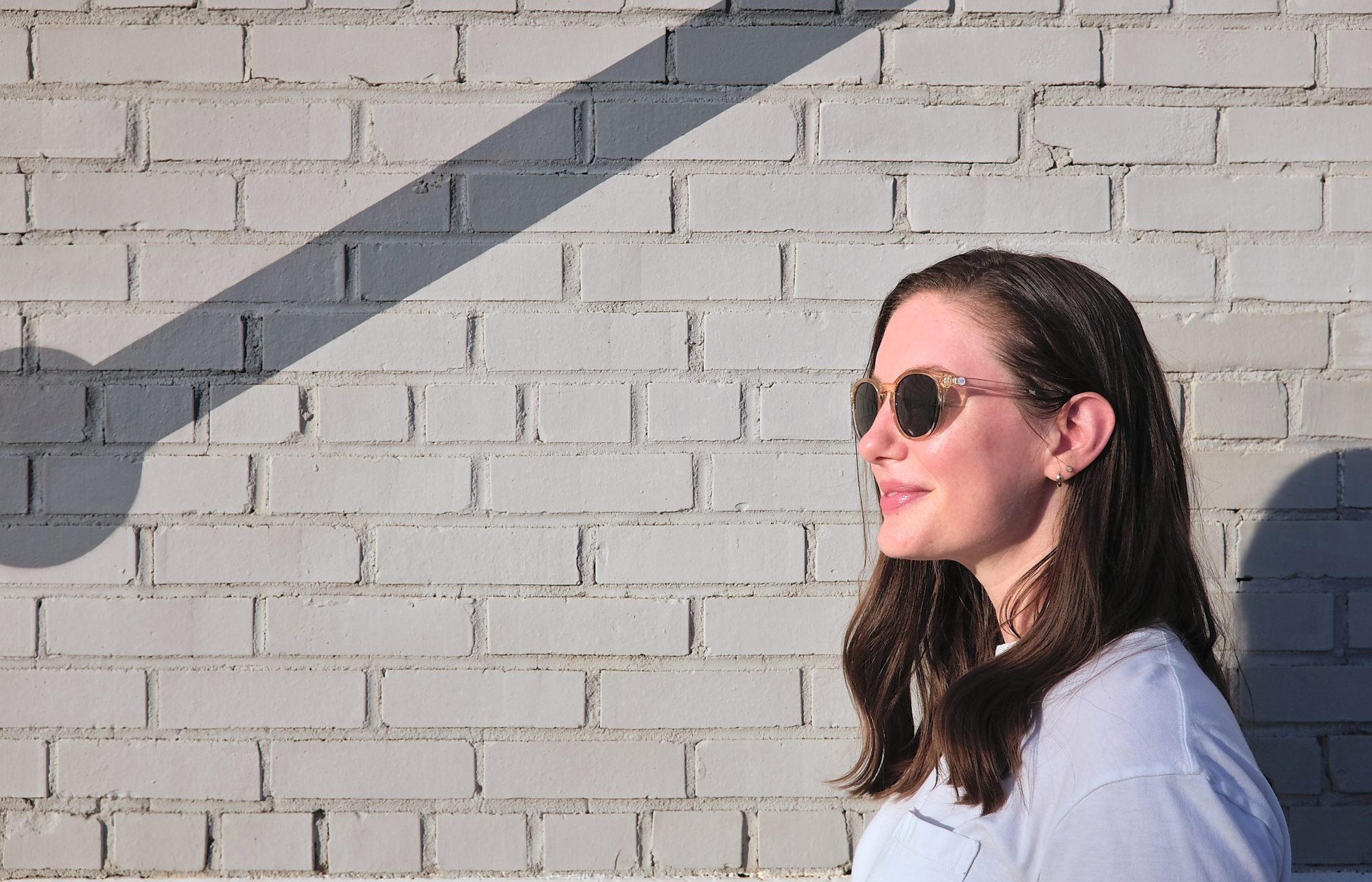 Alyssa wears the Yuba sunglasses in front of a tan brick wall and turns in profile