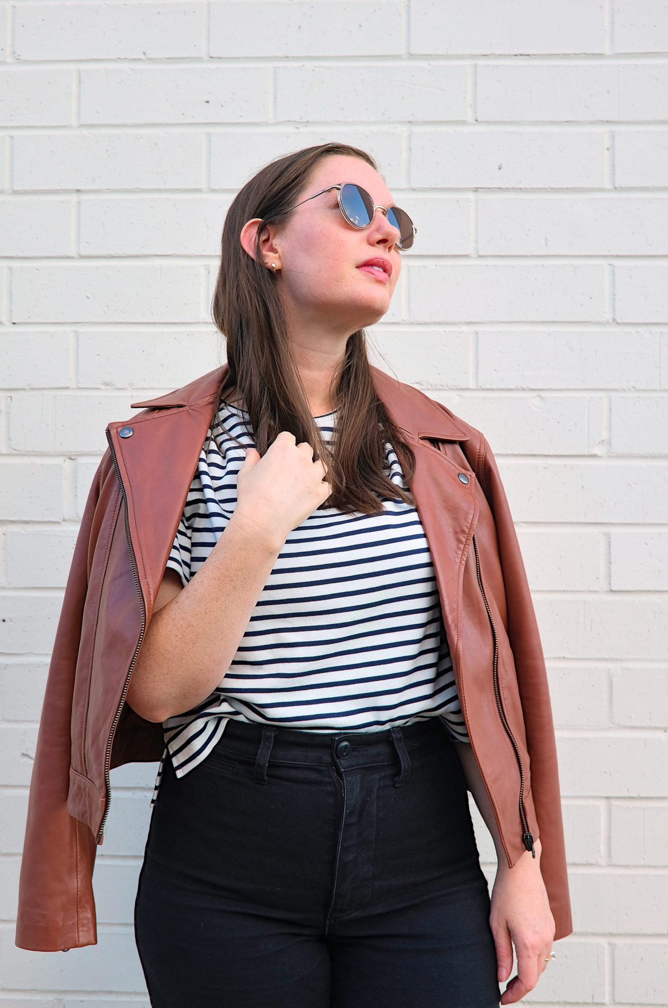 Alyssa wears the Maha Leather Jacket from ABLE with a striped tee; the sky is reflected in her sunglasses