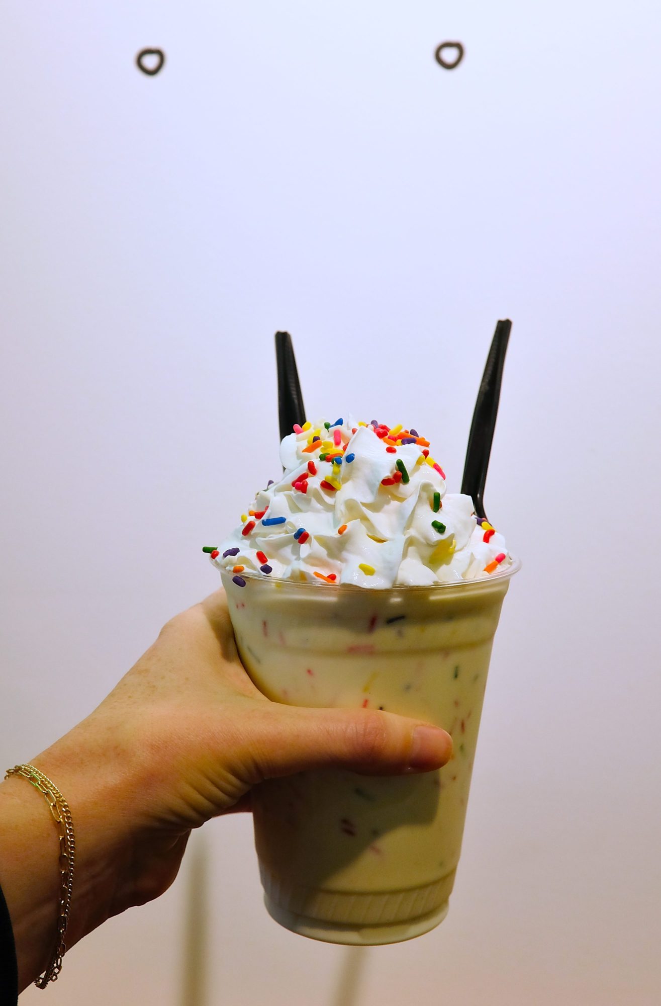 Alyssa holds a milkshake in front of a wall