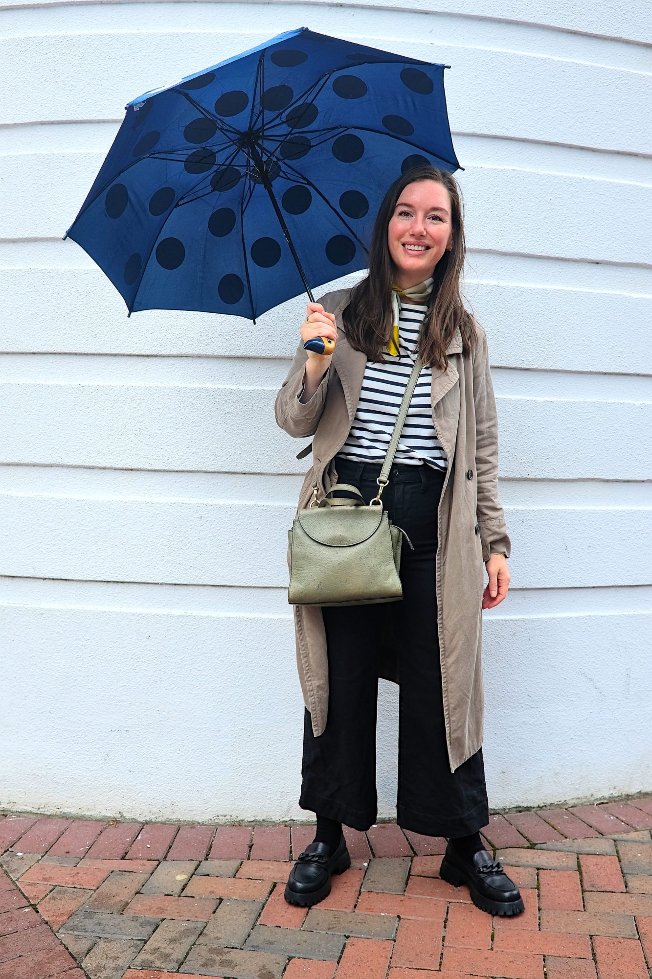 Alyssa holds an umbrella and wears a Breton top with black pants
