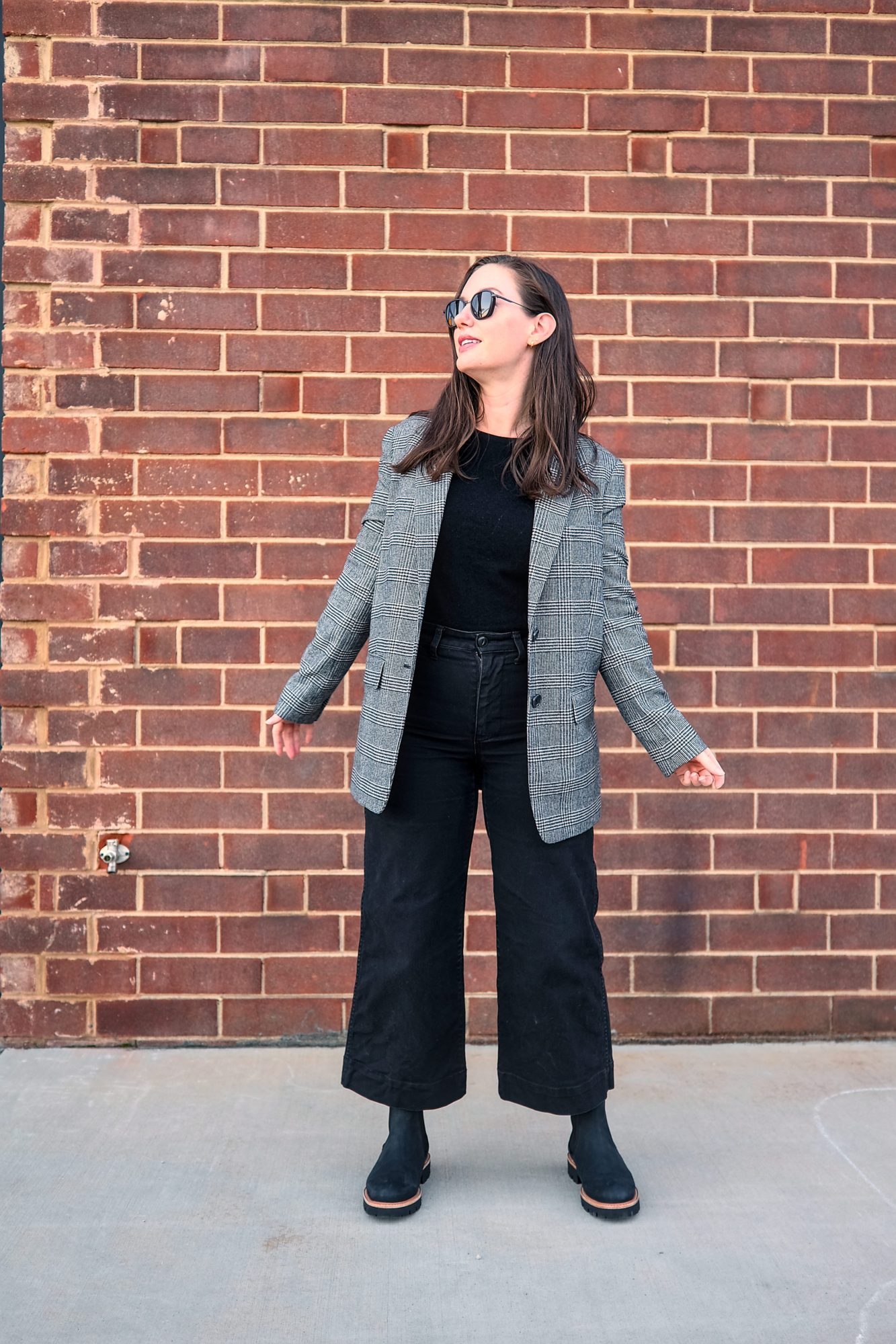 Alyssa wears the Go-To Lug Chelsea Boot with a plaid blazer and black pants in front of a brick wall