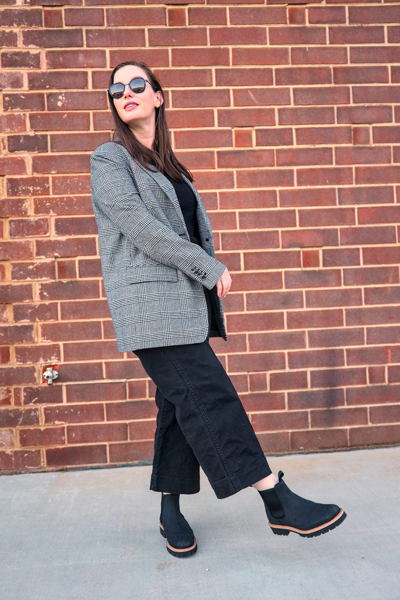 Alyssa wears the Go-To Lug Chelsea Boot with a plaid blazer and black pants and kicks a foot in front of her