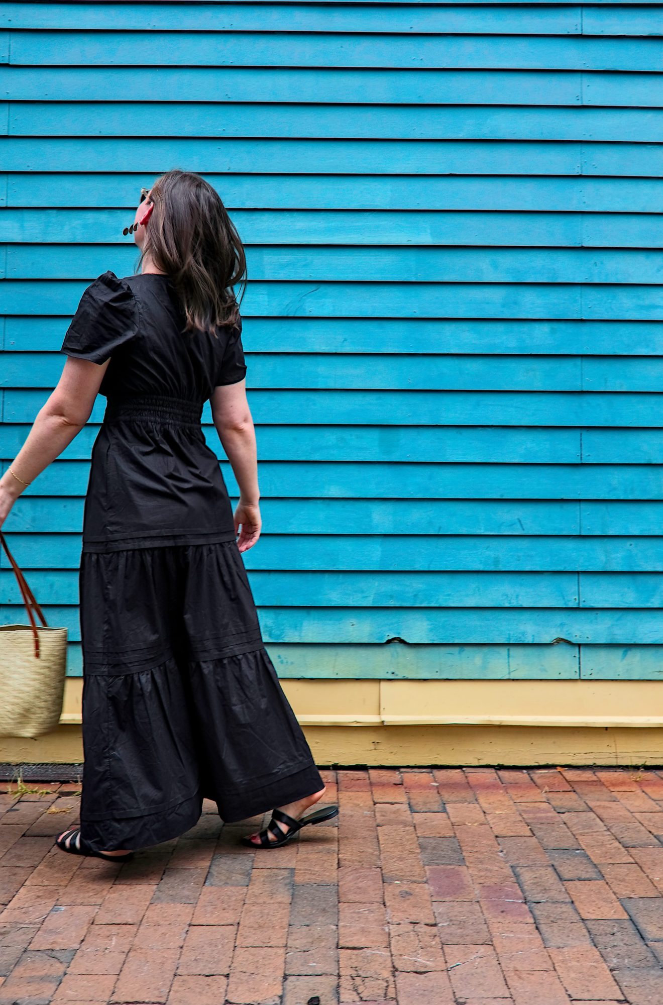 Alyssa wears the Alyssa wears the Quince Cotton Tiered Maxi Dress with sandals and a basket purse and walks out of frame