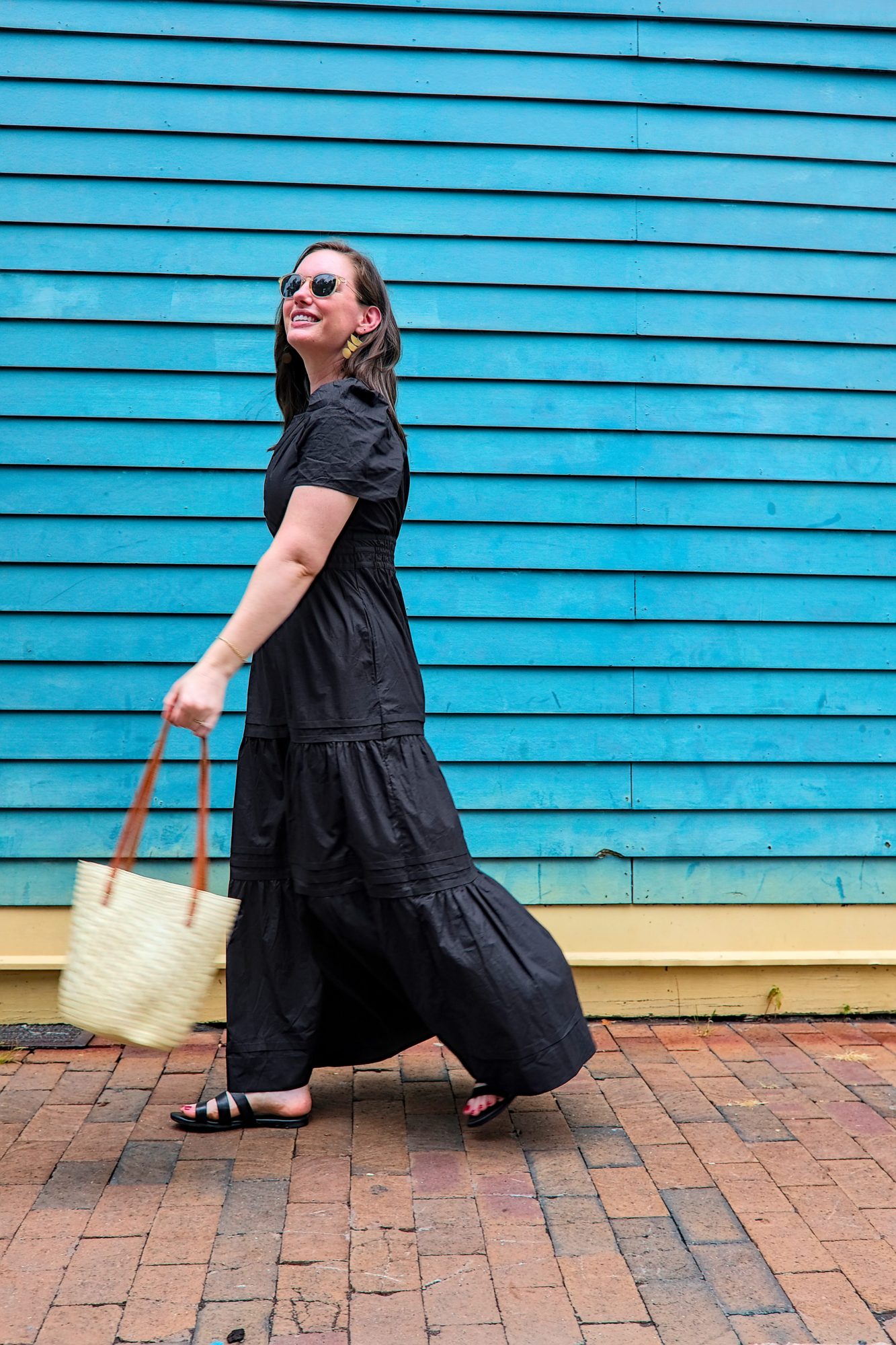 Alyssa wears a black cotton poplin dress from Quince and walks in front of a blue wall