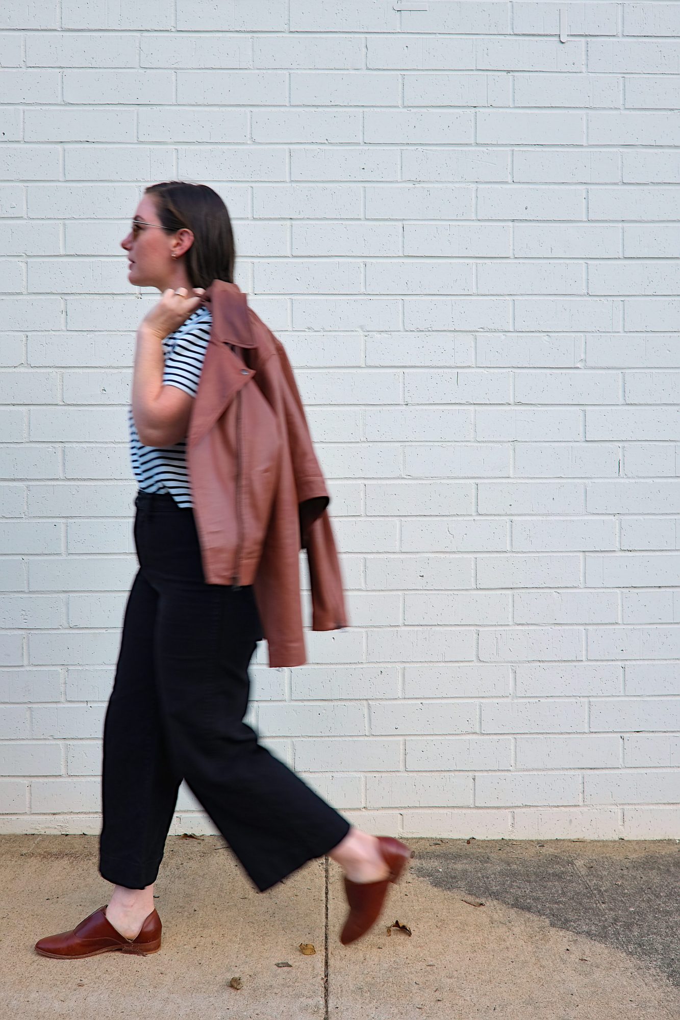 Alyssa walks in front of a brick wall carrying the ABLE Maja leather jacket