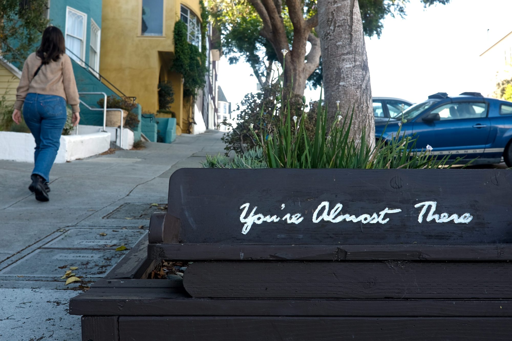 Alyssa walks up a hill in San Francisco and a bench reads "you're almost there"