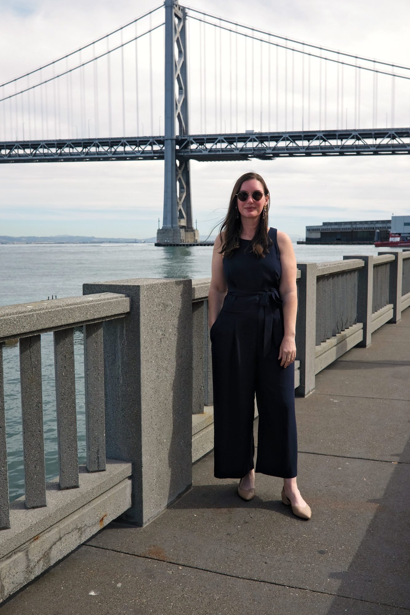 Alyssa wears a navy jumpsuit in front of the Bay Bridge